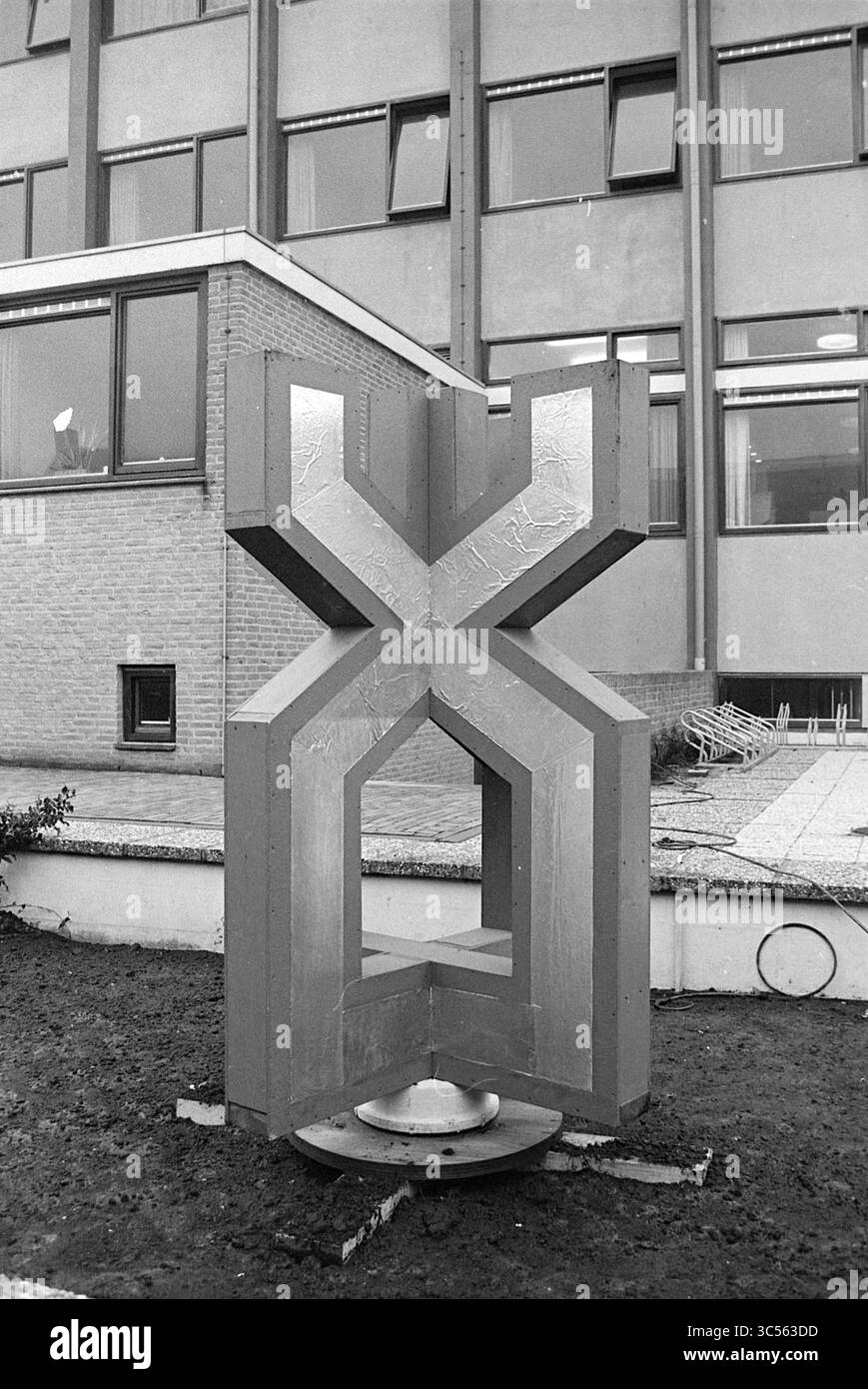 Image Blast Furnace Chess Tournament, 16-01-1968 Whizgle News, Dutch Desk, pays-Bas, 1950-2000 A large, la sculpture abstraite présente un design géométrique saisissant avec un centre ouvert, des lignes nettes contrastées et des surfaces lisses. Il se trouve bien en vue dans un espace extérieur, entouré de lits de plantes soigneusement agencés et adjacent à un bâtiment moderne avec de grandes fenêtres. Banque D'Images