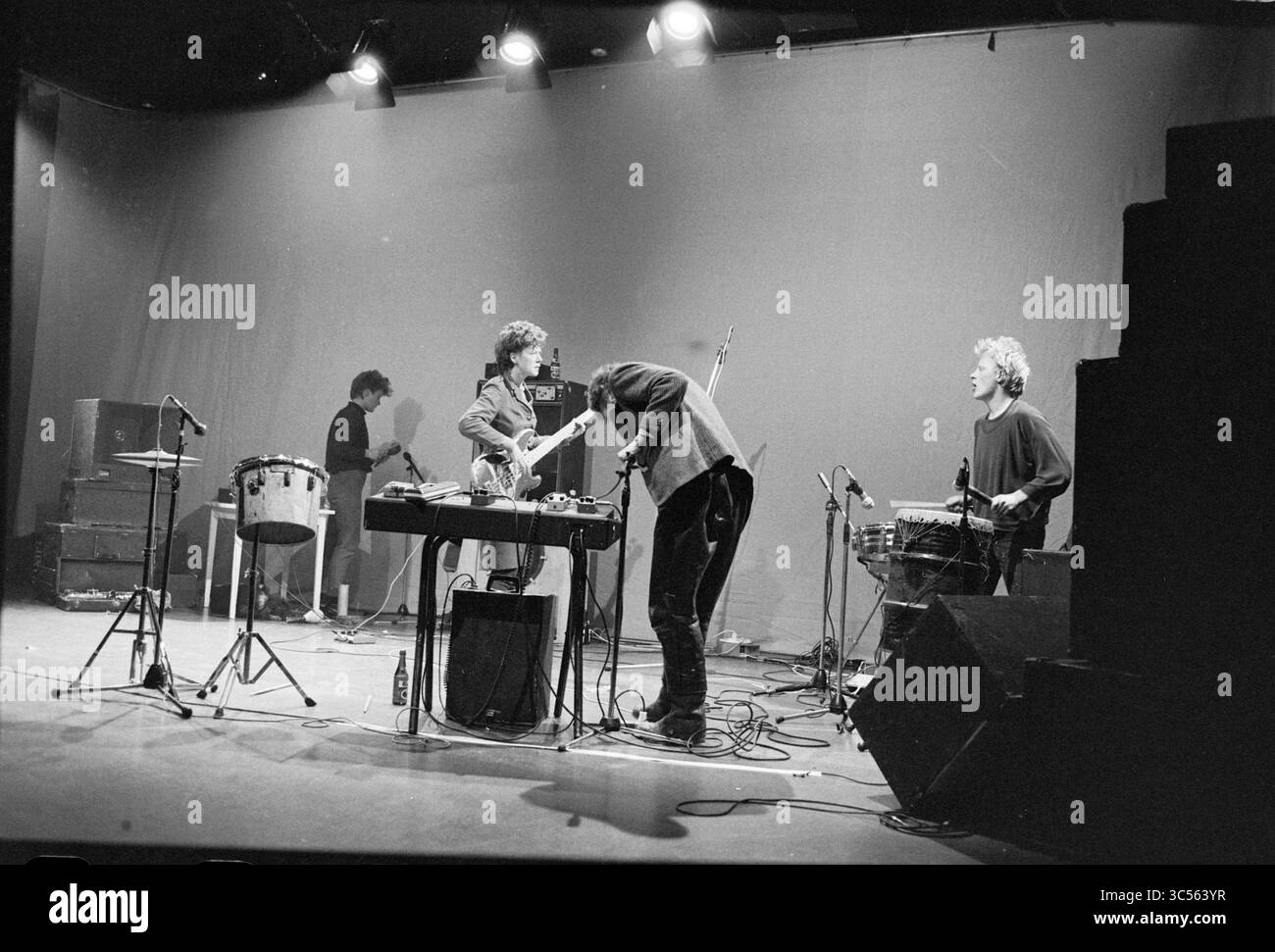 Performance Nexda Witte Tejater, musique, 05-12-1982 Whizgle News, Dutch Desk, pays-Bas, 1950-2000 Un groupe se produit sur scène, entouré de divers instruments et équipements de musique. Les membres sont profondément engagés dans leurs instruments, avec un guitariste penché sur une table d'équipement. L'atmosphère est focalisée et électrique, avec des lumières de scène projetant des ombres dynamiques. Banque D'Images