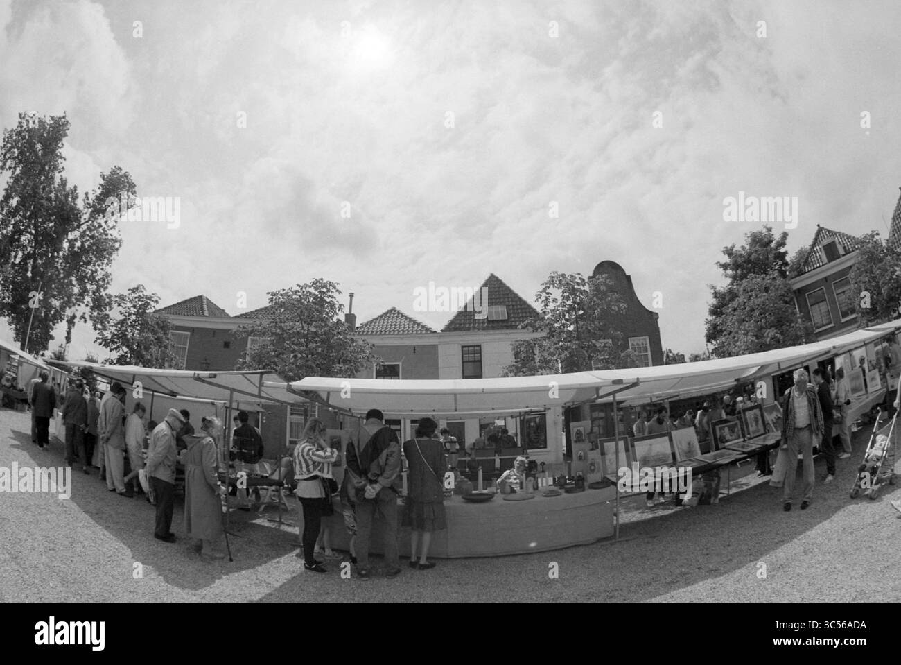 Art Market, Spaarndam, 19-07-1991 Whizgle News, Dutch Desk, pays-Bas, 1950-2000 Un marché en plein air animé présente une variété d'étals présentant des œuvres d'art et des objets artisanaux, avec des visiteurs explorant et engageant avec des vendeurs sous un ciel nuageux. Arbres et bâtiments peuvent être vus en arrière-plan, créant une atmosphère animée. Banque D'Images