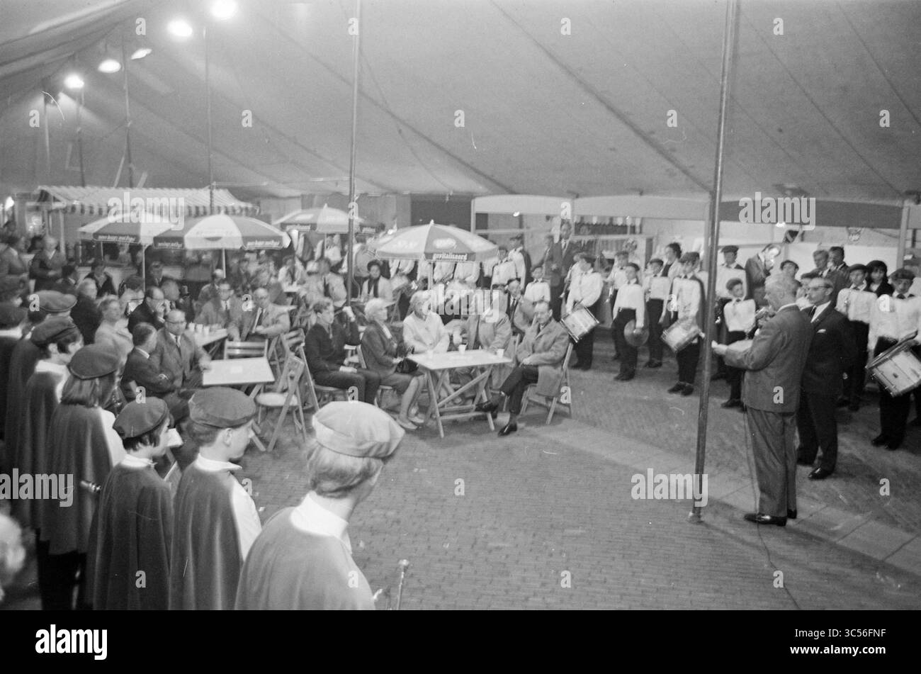 Ouverture du salon des petites entreprises, ouverture, ouvertures, mise en service, 31-05-1967 Whizgle News, Dutch Desk, pays-Bas, 1950-2000 Un rassemblement animé sous une grande tente, avec un public assis à des tables et une fanfare en uniforme, se produisant devant une foule captivée. Des tables recouvertes de parasols préparent le décor de cet événement festif, où un conférencier s'entretient avec les participants. Banque D'Images