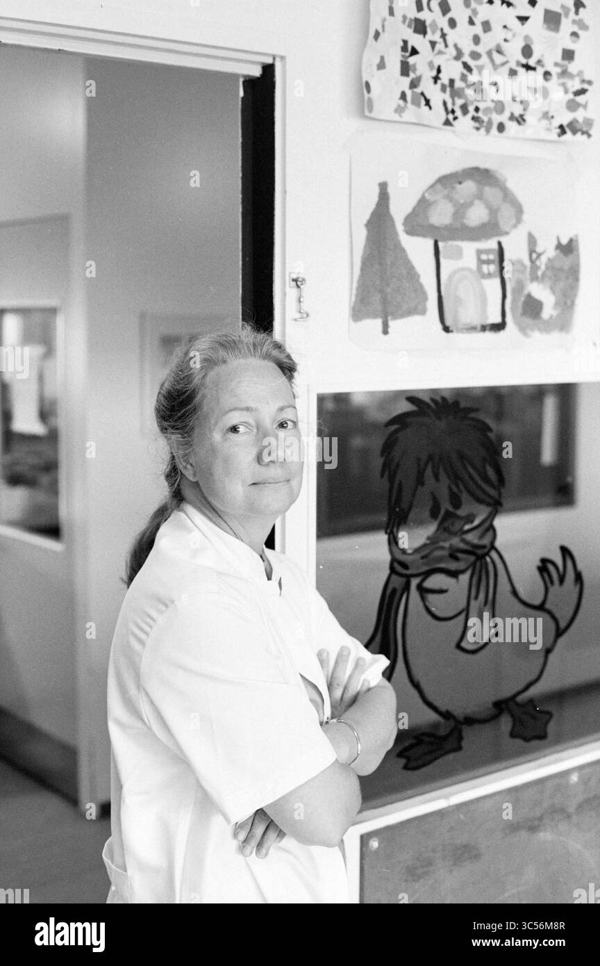 Pédiatre Dr Hammond, EG [Elisabeth Gasthuis], 06-05-1992 Whizgle News, Dutch Desk, pays-Bas, 1950-2000 Une femme souriante vêtue d'un manteau blanc se tient debout, les bras croisés, positionnée à côté d'œuvres d'art colorées pour enfants, y compris un dessin fantaisiste d'un canard. L'atmosphère suggère un environnement stimulant et créatif, probablement dans une école ou une garderie. Banque D'Images