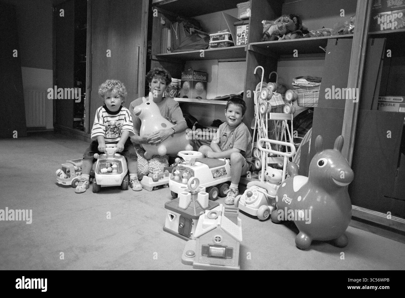 Speel-o-theek Kindervreugd, Hillegom, 22-06-1990 Whizgle News, Dutch Desk, pays-Bas, 1950-2000 deux enfants sont assis sur le sol, entourés d'une panoplie de jouets colorés. Un enfant a les cheveux bouclés et se concentre sur une voiture jouet, tandis que l'autre tient un animal en peluche. Derrière eux, les étagères sont remplies de plus de jouets, créant une atmosphère ludique et joyeuse. Banque D'Images