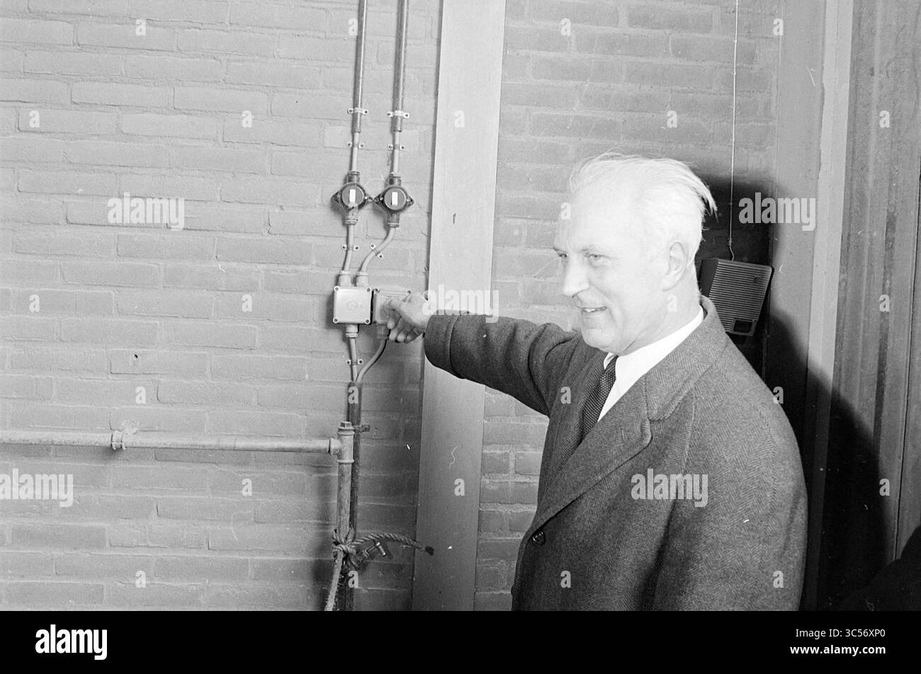 Ouverture installation de broyage de saleté, ouverture, ouvertures, mise en service, 01-04-1969 Whizgle News, Dutch Desk, pays-Bas, 1950-2000 Un homme vêtu d'un manteau formel se tient près d'un mur, pointant vers un petit appareil relié à un système de vannes et de tuyaux. Il semble engagé et bien informé, discutant probablement de la fonction de l'équipement ou en faisant la démonstration. Banque D'Images
