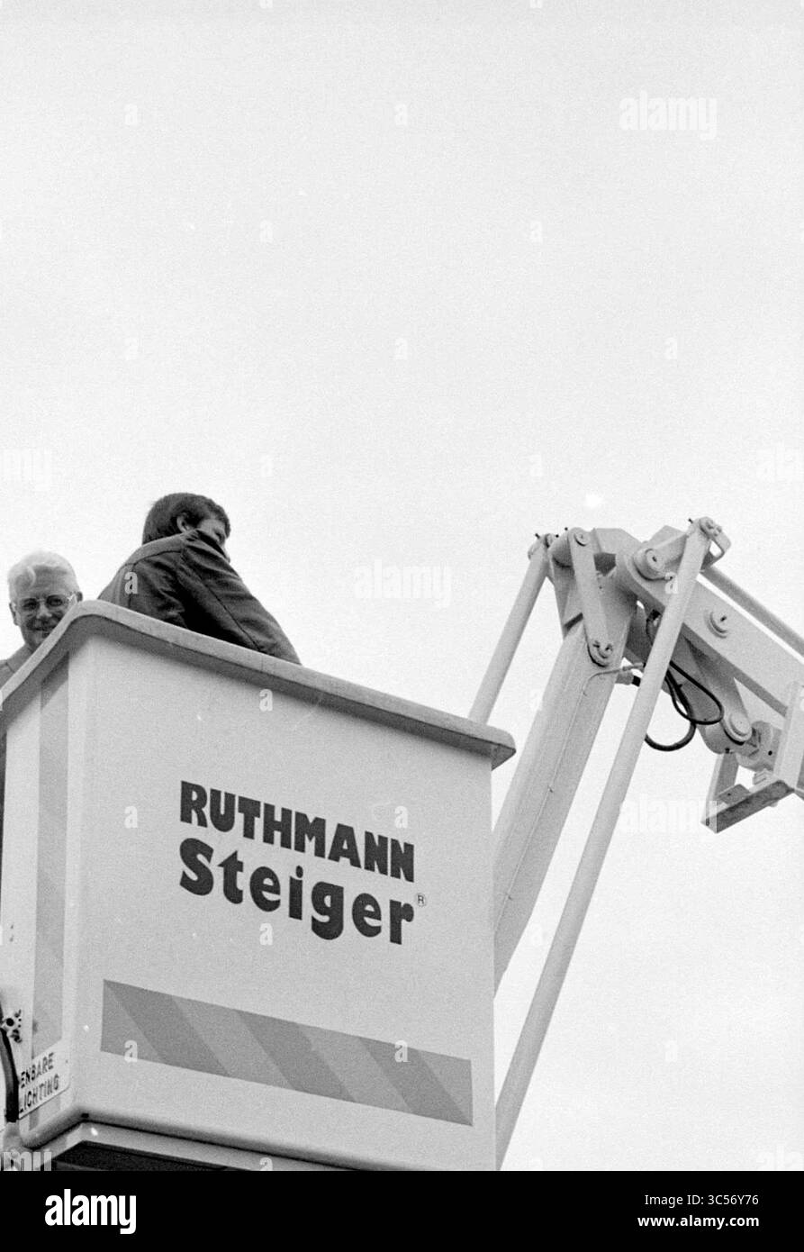 Remise de plate-forme de travail aérien, Heemskerk, remise et transferts, Heemskerk, 17-08-1979 Whizgle News, Dutch Desk, pays-Bas, 1950-2000 deux individus sont assis sur une plate-forme surélevée, surplombant leur environnement. Une personne se penche légèrement sur le bord, tandis que l'autre est enveloppée dans une veste, les deux semblant engagés dans la conversation ou l'observation. La plate-forme est soutenue par un bras mécanique, faisant allusion à une construction ou à une configuration d'événement en cours. Banque D'Images