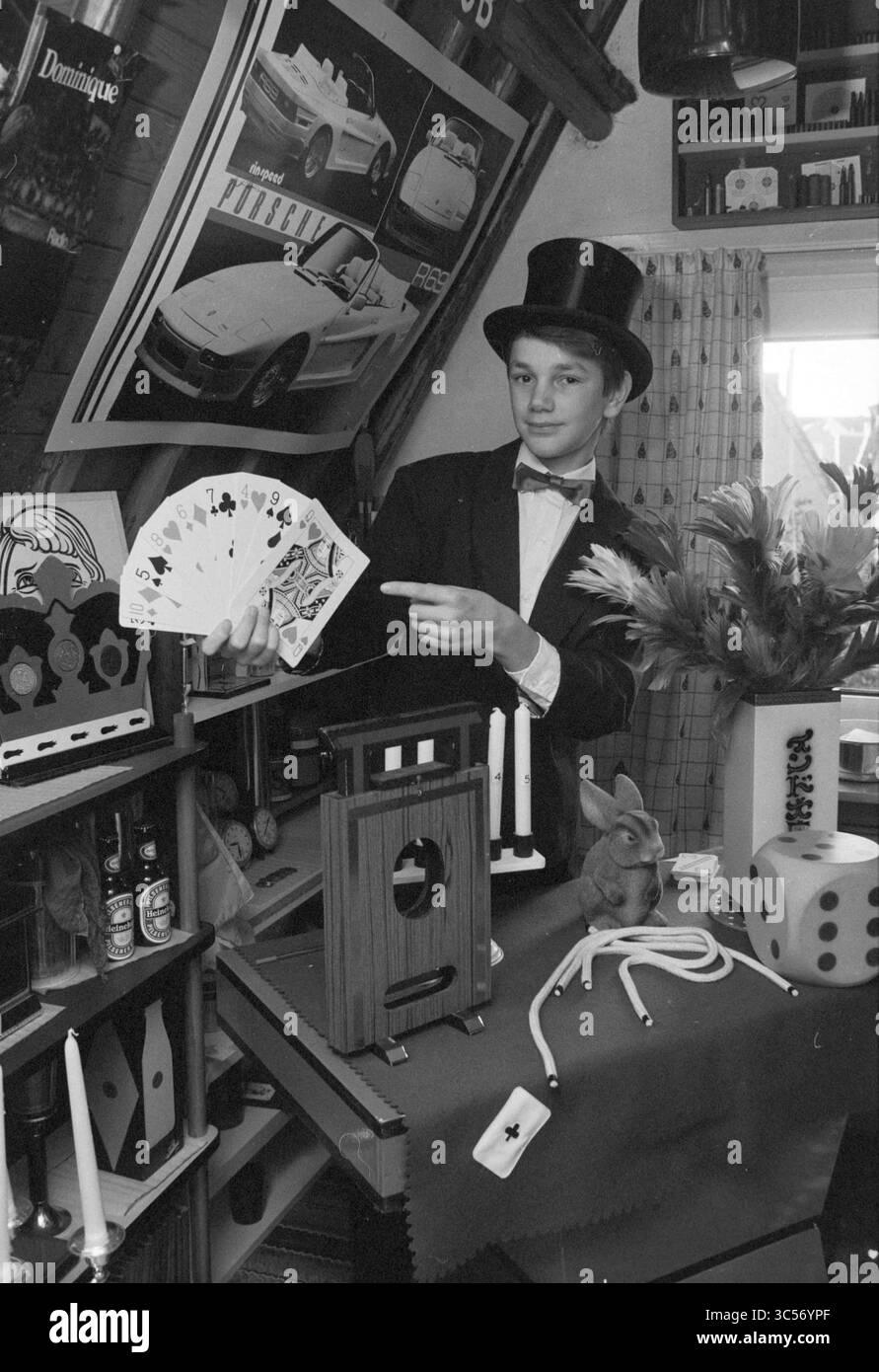 Bart van Capelle, magicien, 14 ans, Magic, 24-10-1989 Whizgle News, Dutch Desk, pays-Bas, 1950-2000 Un jeune magicien en tenue formelle tient un jeu de cartes à jouer, faisant des gestes en toute confiance pendant qu'il exécute un tour. La scène est remplie d'accessoires comme un petit lapin, des bougies et des dés, le tout sur fond d'affiches et de curiosités diverses, ajoutant à l'atmosphère d'enchantement et de mystère. Banque D'Images