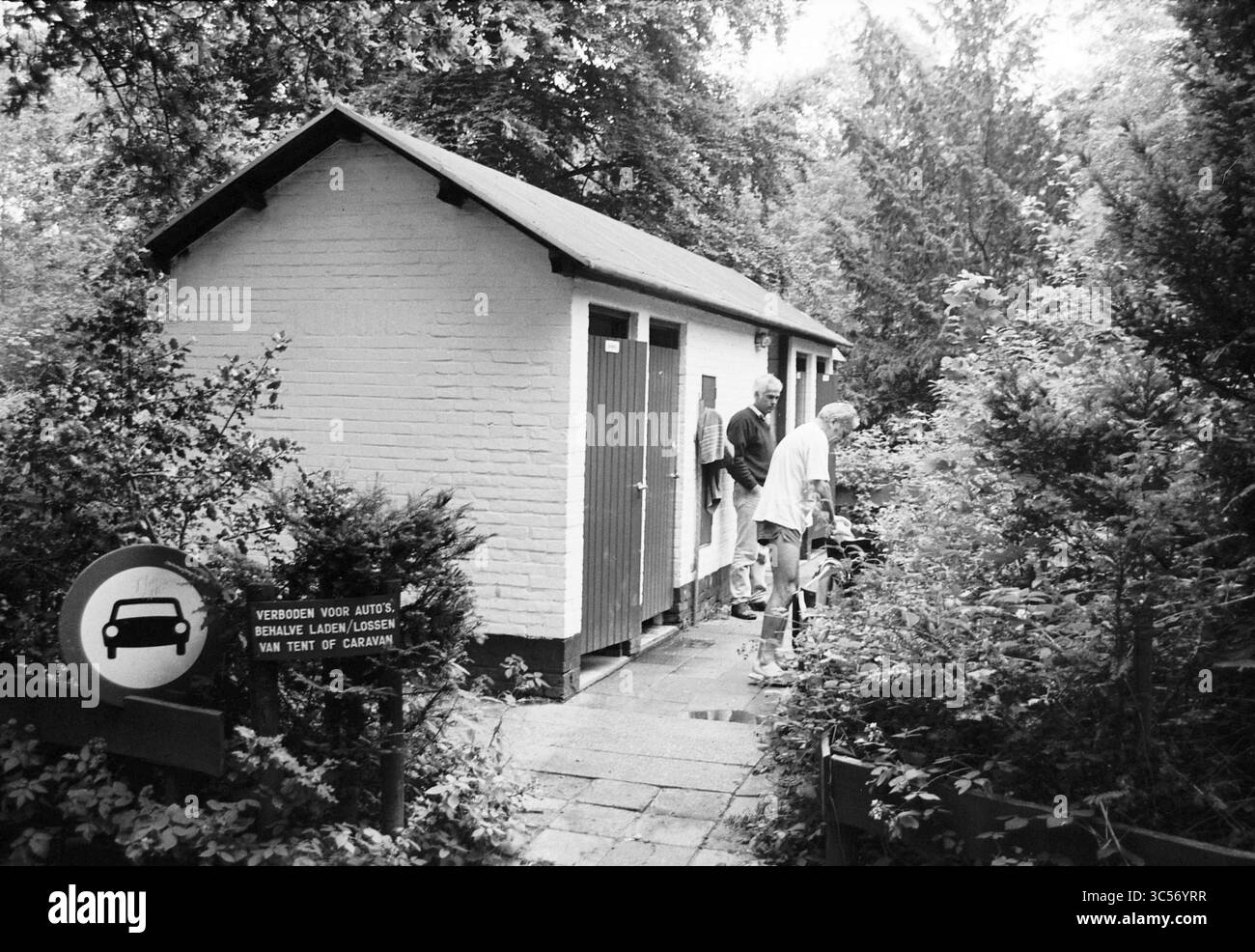 Douche au camping Schoonenberg, Velsen-Zuid, Driehuizerkerkweg, 24-07-1996 Whizgle News, Dutch Desk, pays-Bas, 1950-2000 deux personnes se tiennent devant un petit bâtiment entouré de verdure, avec une personne appuyée contre la porte. Un panneau à proximité indique les restrictions de stationnement, suggérant qu'il s'agit d'un camping ou d'une zone de loisirs. La scène transmet un cadre paisible et naturel. Banque D'Images