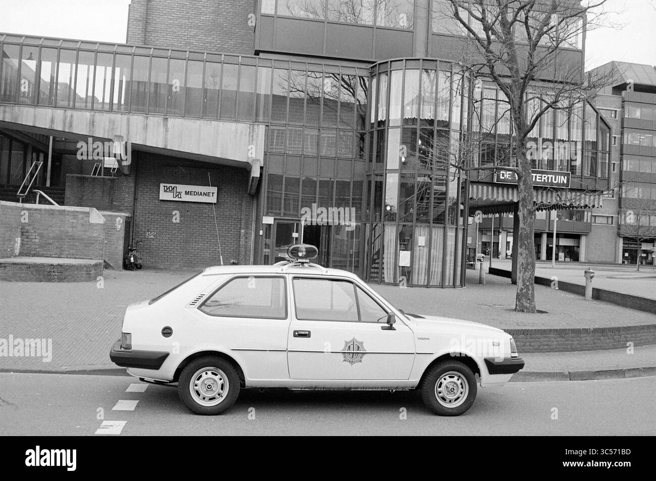 Voiture de police pour Medianet sur Stationsplein Haarlem, Haarlem, Stationsplein, pays-Bas, 00-05-1982 Whizgle News, Dutch Desk, pays-Bas, 1950-2000 Une voiture de police compacte est garée devant un bâtiment moderne avec de grandes fenêtres en verre et une entrée distinctive, créant un contraste entre le véhicule et l'architecture. Banque D'Images
