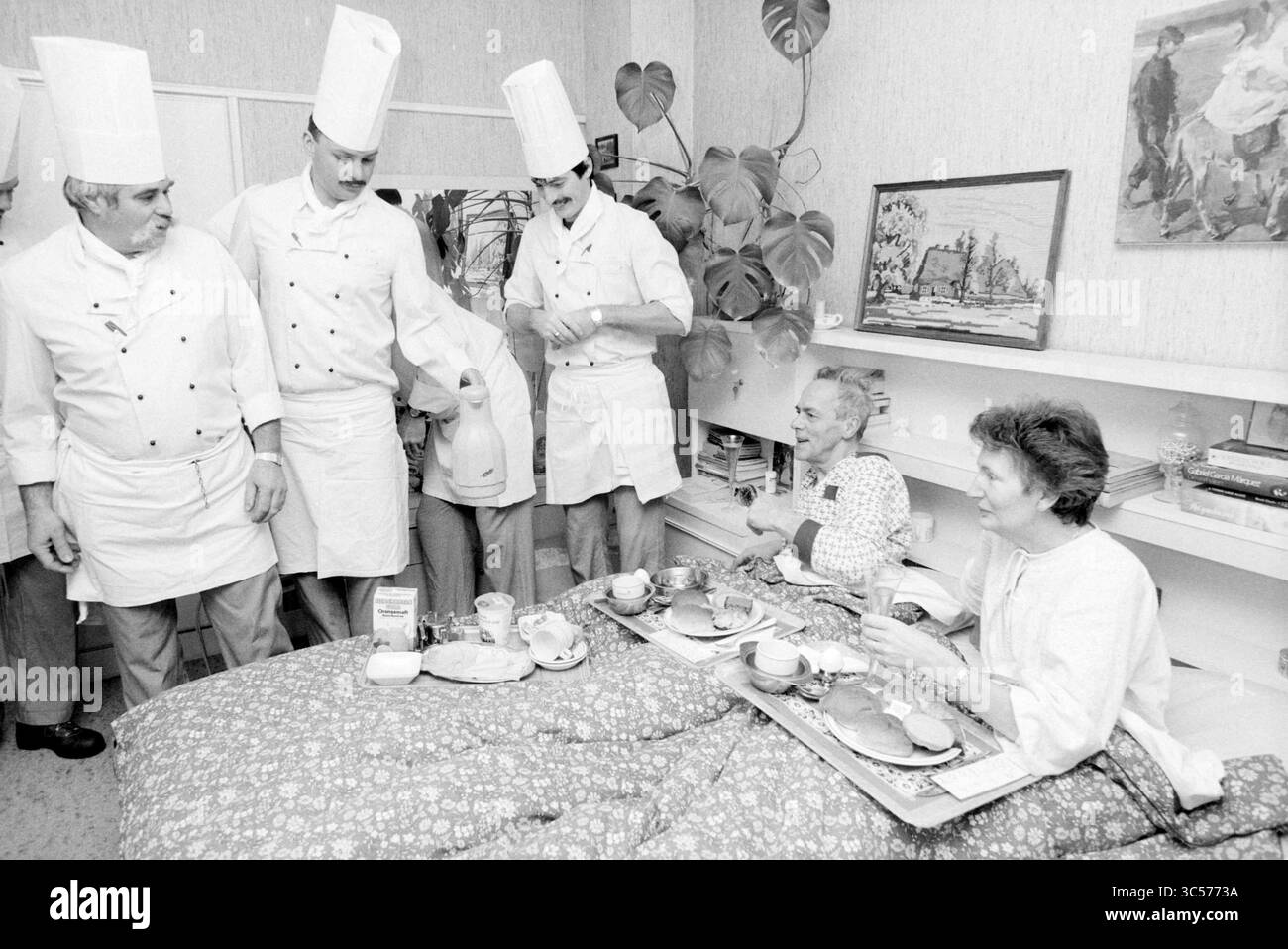 Petit déjeuner pour Mr. Morssink, H'lem, nourriture et restaurants, Haarlem, pays-Bas, 04-01-1990 Whizgle News, Dutch Desk, pays-Bas, 1950-2000 Un groupe de chefs en uniforme blanc traditionnel sert le petit déjeuner à deux invités assis dans une salle confortable, mettant en valeur une interaction chaleureuse et une atmosphère accueillante. Les plateaux de table sont remplis de divers articles pour le petit-déjeuner, créant un sentiment de confort et de soin. Banque D'Images