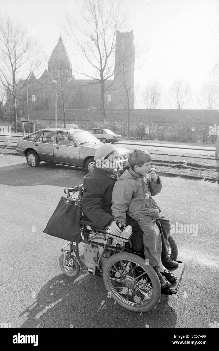 Annemiek + Michaël en fauteuil roulant, Haarlem, 08-03-1993 Whizgle News, Dutch Desk, pays-Bas, 1950-2000 Une personne dans un fauteuil roulant motorisé porte un enfant, souriant tous les deux lorsqu'ils naviguent dans la rue. En arrière-plan, un bâtiment historique et des arbres se dressent en hauteur, tandis qu'une voiture garée ajoute à la scène urbaine. Banque D'Images