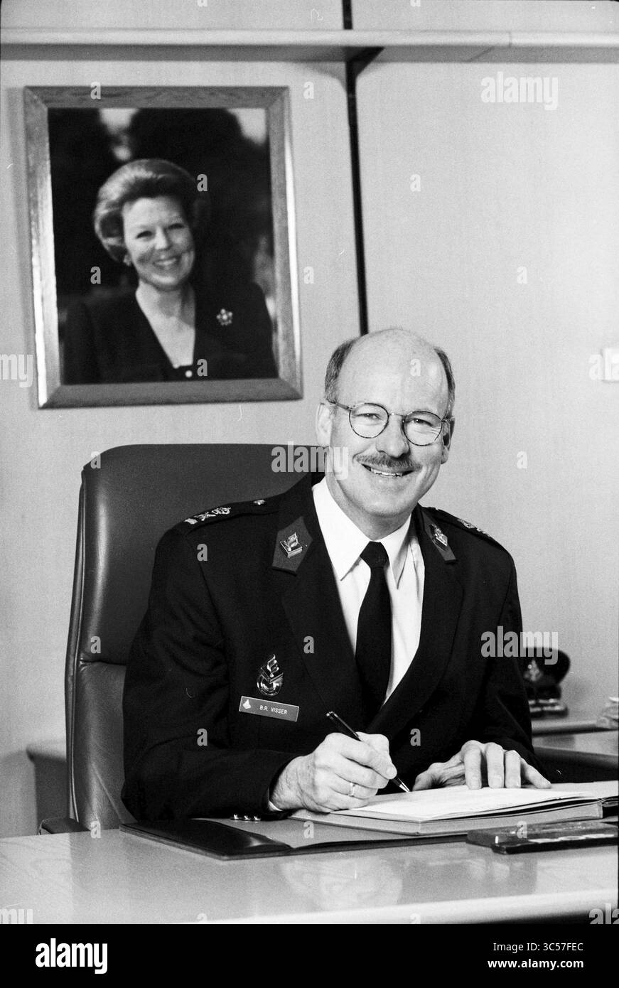 Portraits Chef de la police Haarlem, Haarlem, pays-Bas, 02-12-1997 Whizgle News, Dutch Desk, pays-Bas, 1950-2000 Un homme en uniforme militaire est assis à un bureau, souriant en écrivant. Derrière lui se trouve un portrait encadré d'une femme, suggérant une position d'autorité ou de reconnaissance. Le cadre transmet un sens du professionnalisme et du respect. Banque D'Images