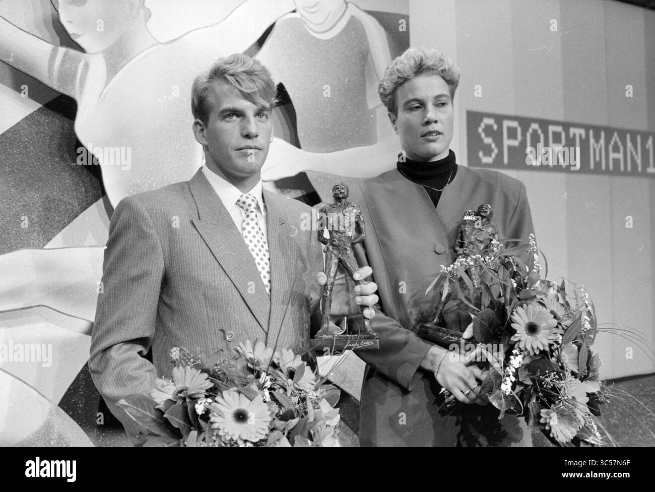Sportif/femme de l'année, H'veen, Heerenveen, 12-12-1991 Whizgle News, Dutch Desk, pays-Bas, 1950-2000 Un homme et une femme se tiennent fièrement debout, chacun tenant un trophée, entourés d'arrangements floraux. Ils sont habillés en tenue formelle, indiquant un événement de célébration. L'arrière-plan présente des figures abstraites en mouvement, suggérant un thème sportif. Banque D'Images