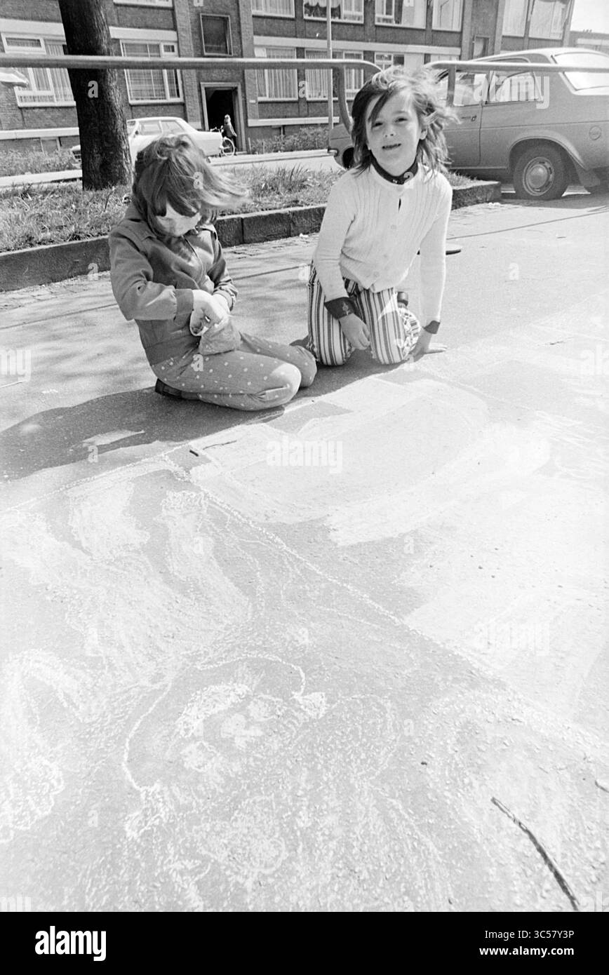 Panneaux de signalisation à plantage, Beverwijk, Queen's Day, Beverwijk, plantage, pays-Bas, 30-04-1975 Whizgle News, Dutch Desk, pays-Bas, 1950-2000 deux enfants sont agenouillés sur le sol, dessinant joyeusement à la craie. Un enfant se concentre sur la création d'art, tandis que l'autre lève les yeux, souriant. En arrière-plan, une voiture est garée à côté d'un bâtiment avec plusieurs fenêtres, donnant un aperçu d'un quartier animé. Banque D'Images