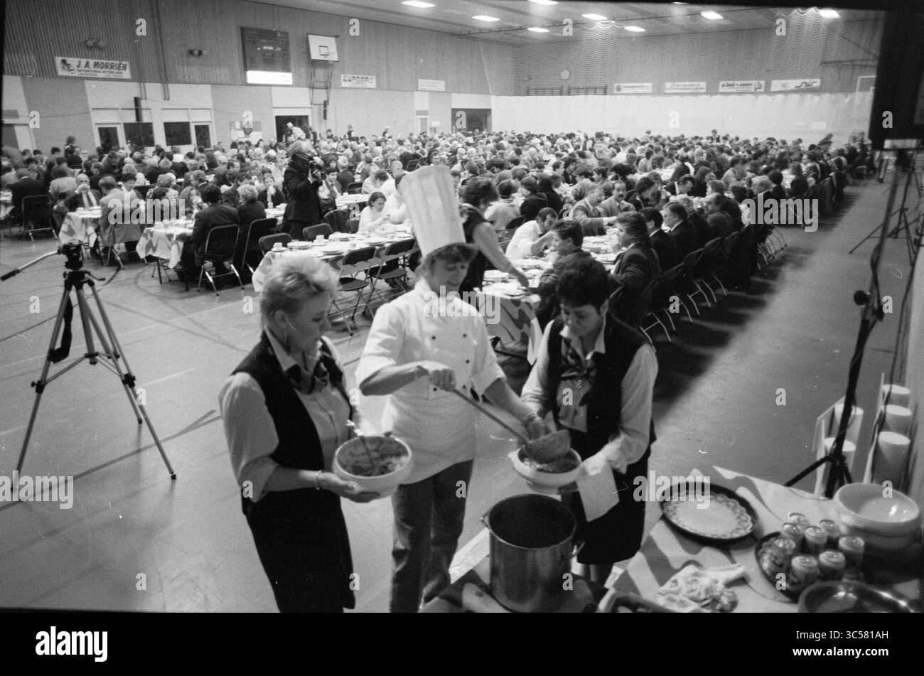 Cérémonie de remise des prix Hoogovens Chess Tournament, Wijk aan Zee, 02-02-1991 Whizgle News, Dutch Desk, pays-Bas, 1950-2000 Une scène de banquet animée avec une foule nombreuse réunie pour un repas, avec des serveurs servant de la nourriture dans de grands bols au premier plan. L'atmosphère est animée, mettant en valeur une célébration commune et les efforts du personnel de service dévoué. Banque D'Images
