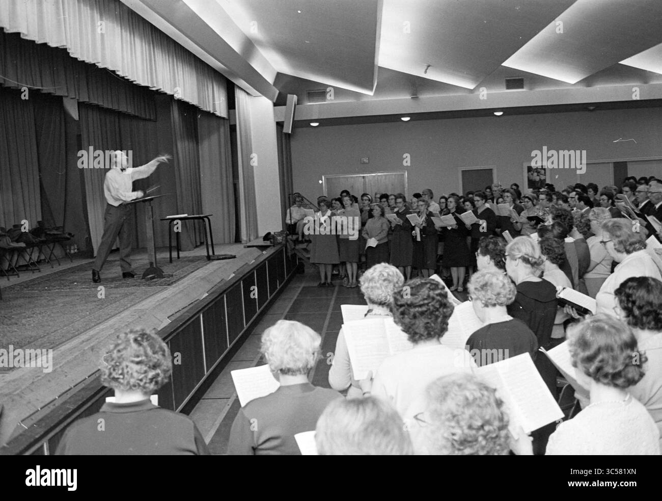 Répétition de choeur Hildebrandzaal, répétition, 26-04-1969 Whizgle News, Dutch Desk, pays-Bas, 1950-2000 Un chef d'orchestre dirige un grand groupe de chanteurs lorsqu'ils se rassemblent pour pratiquer, tandis que la musique en feuille est tenue dans leurs mains. L'atmosphère vibrante suggère un événement communautaire rempli d'enthousiasme et de collaboration. Banque D'Images Répétition de choeur Hildebrandzaal, répétition, 26-04-1969 Whizgle News, Dutch Desk, pays-Bas, 1950-2000 Un chef d'orchestre dirige un grand groupe de chanteurs lorsqu'ils se rassemblent pour pratiquer, tandis que la musique en feuille est tenue dans leurs mains. L'atmosphère vibrante suggère un événement communautaire rempli d'enthousiasme et de collaboration. Banque D'Images
