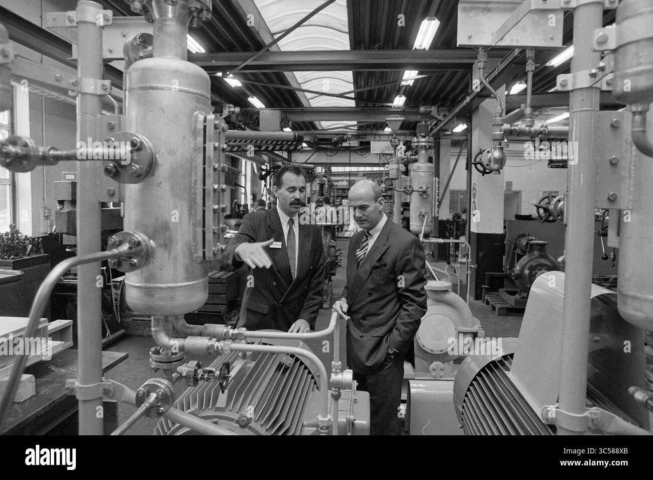 Ouverture d'une usine de pompes, Zwanenburg, 13-04-1994 Whizgle News, Dutch Desk, pays-Bas, 1950-2000 deux hommes participent à une discussion tout en examinant des machines industrielles, entourés d'un ensemble de tuyaux et d'équipements. Un homme fait des gestes vers une composante, soulignant un point, tandis que l’autre écoute attentivement, indiquant une exploration collaborative de la technologie. Banque D'Images