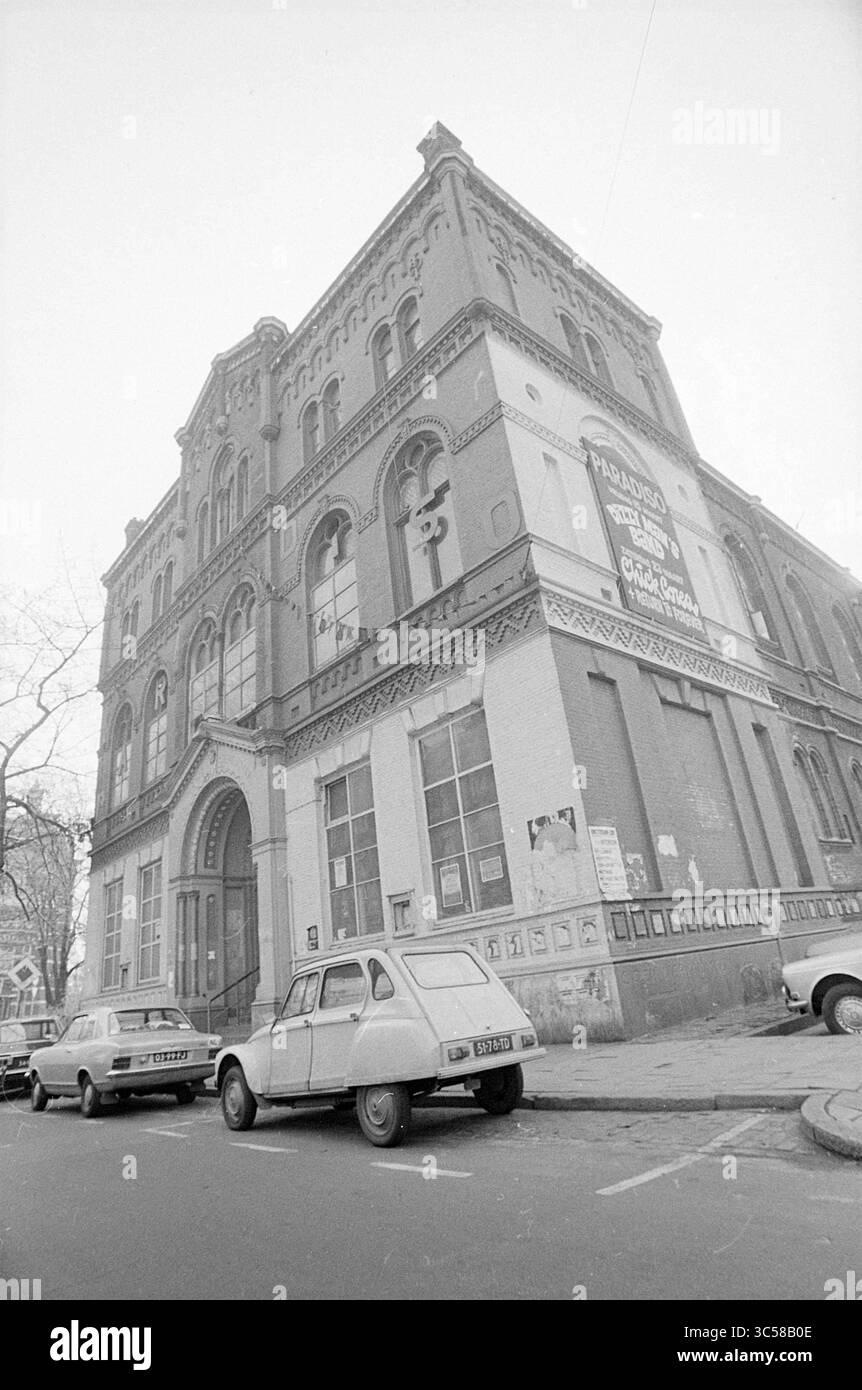 Ext. Paradiso, extérieur, 19-03-1974 Whizgle News, Dutch Desk, pays-Bas, 1950-2000 Un grand bâtiment historique avec des détails architecturaux complexes, avec des fenêtres cintrées et des éléments décoratifs. Les voitures classiques sont garées à côté, faisant allusion à une époque passée, tandis que les affiches ornent les murs extérieurs, suggérant une utilisation et un engagement communautaires actifs. Banque D'Images