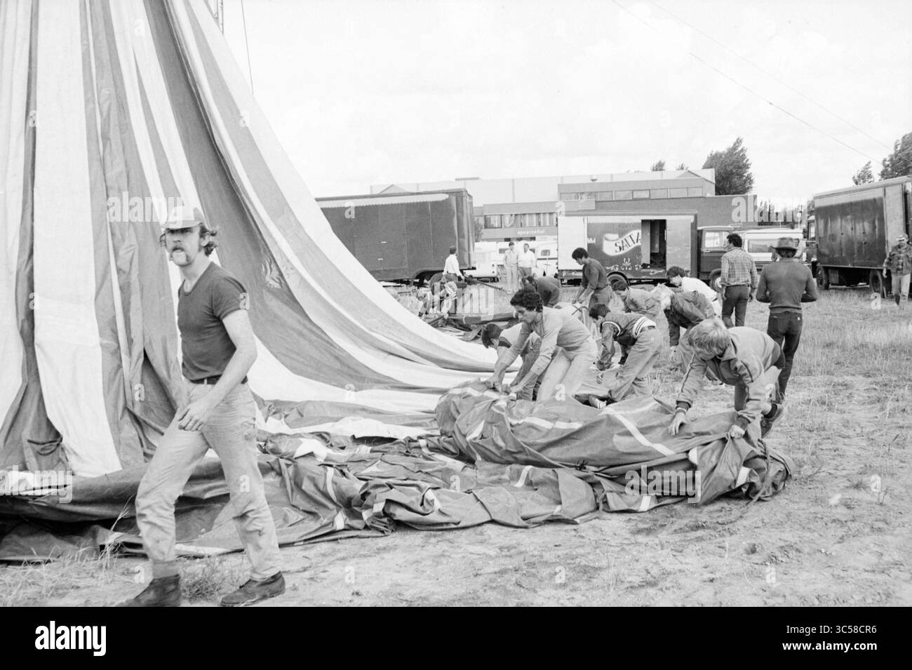 Construire une tente, cirque Saltarino, cirque, 19-08-1982 Whizgle News, Dutch Desk, pays-Bas, 1950-2000 Un groupe de travailleurs est vu préparer et assembler une grande toile, probablement pour un événement ou un festival, avec plusieurs camions garés en arrière-plan. Un homme sourit à la caméra tandis que d'autres sont concentrés sur leurs tâches. Banque D'Images