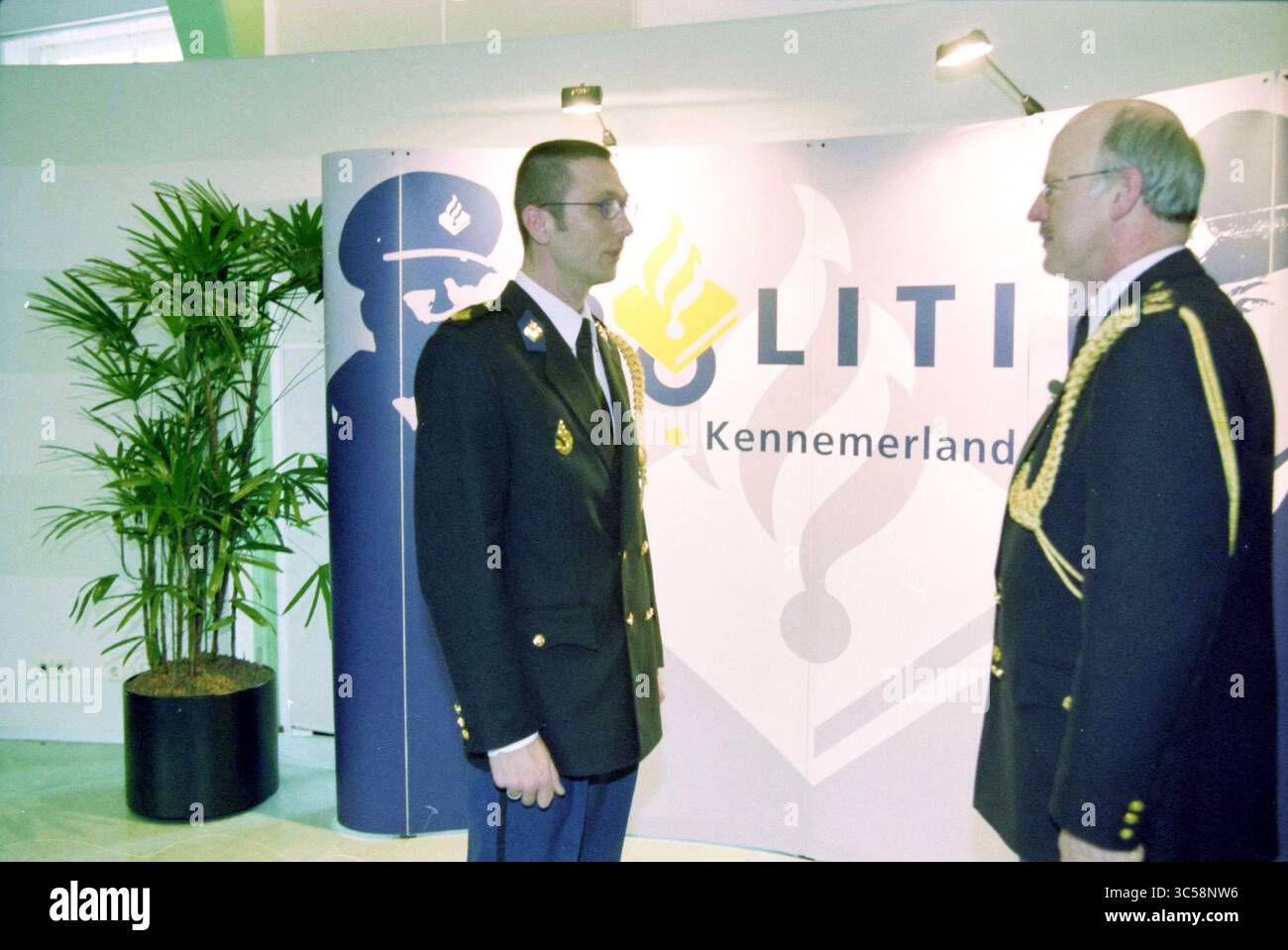 Officiers assermentés, Haarlem, pays-Bas, 26-02-2001 Whizgle News, Dutch Desk, pays-Bas, 1950-2000 deux individus en tenue de cérémonie engagent une conversation près d'un fond arborant un logo lié à l'application de la loi, avec une petite plante en pot à proximité. Banque D'Images
