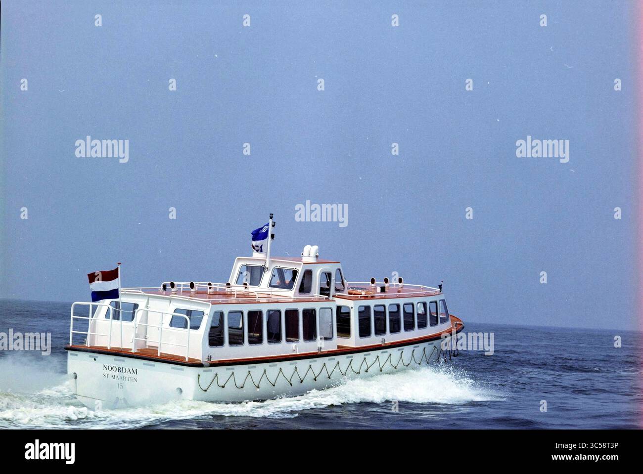 Appel d'offres Noordam, Mulder et Rijke, 24-06-1983 Whizgle News, Dutch Desk, pays-Bas, 1950-2000 Un charmant bateau à passagers glisse dans des eaux calmes, arborant des drapeaux alors qu'il navigue dans le paysage serein. La conception dispose d'une terrasse spacieuse et d'une forme distinctive, ce qui en fait une vue délicieuse sur la toile de fond de l'eau. Banque D'Images