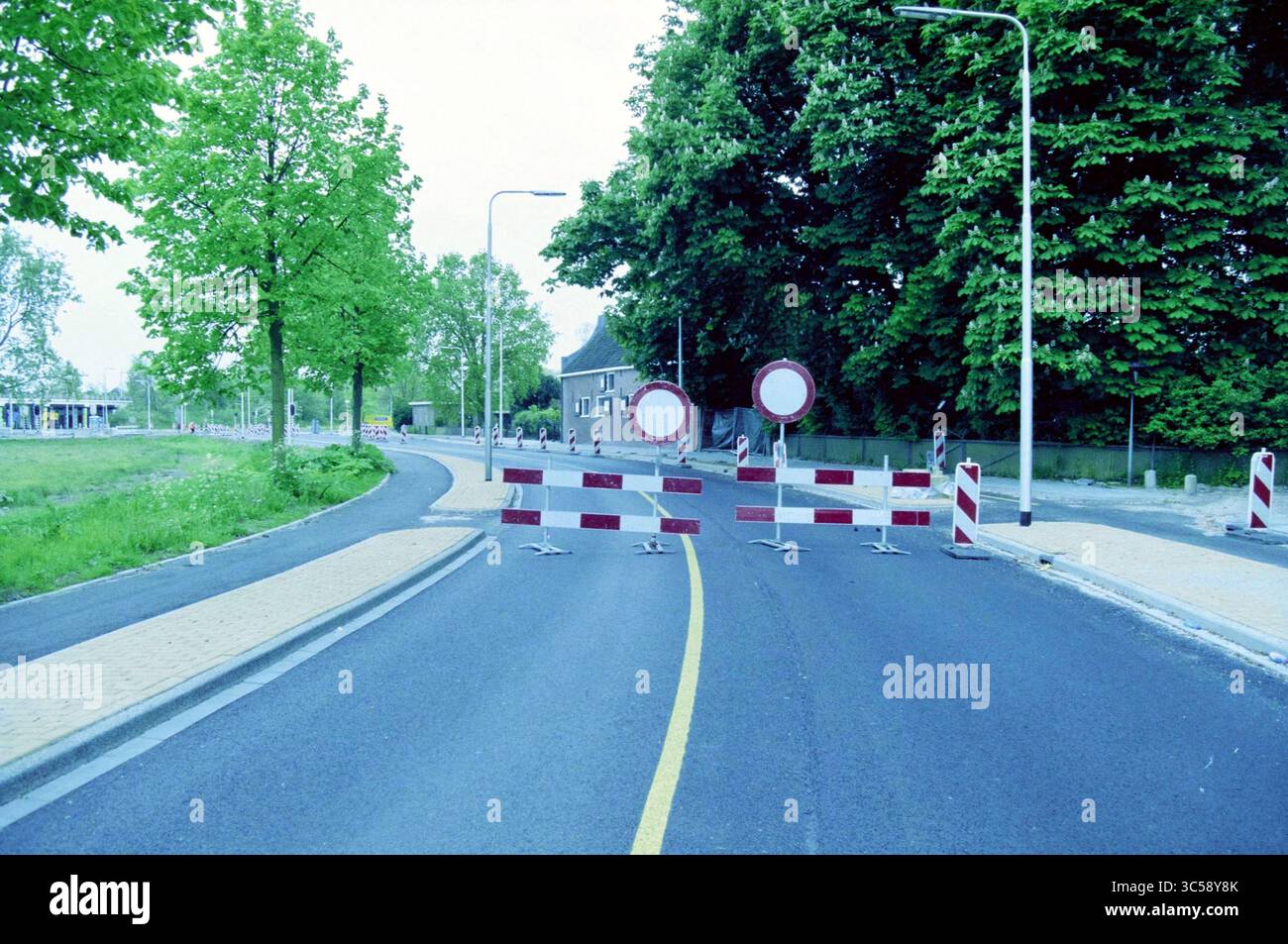 Fermé A208, Haarlem, pays-Bas, 12-05-2002 Whizgle News, Dutch Desk, pays-Bas, 1950-2000 Une route est bloquée par une série de barrières, avec des panneaux circulaires indiquant l'interdiction d'entrée. Des arbres luxuriants bordent les côtés de la rue et un bâtiment est visible en arrière-plan, créant un contraste entre nature et développement urbain. Banque D'Images
