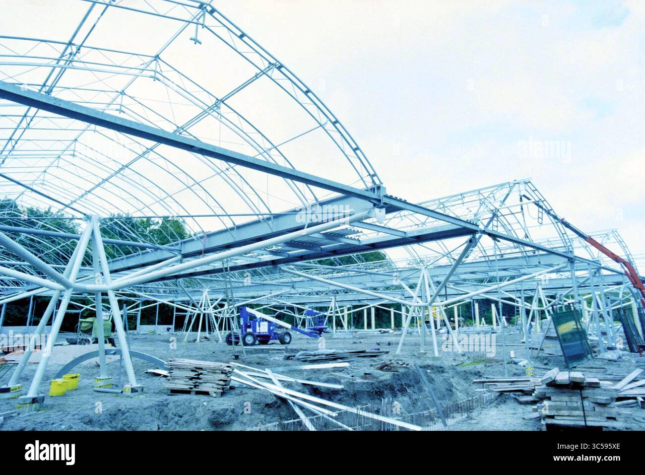 Construction de l'espace d'exposition Keukenhof, 29-08-1996 Whizgle News, Dutch Desk, pays-Bas, 1950-2000 structure incomplète avec une ossature de poutres et d'arches métalliques, entourée de matériaux et d'équipements de construction sur une surface de gravier, posée contre un ciel nuageux. Banque D'Images