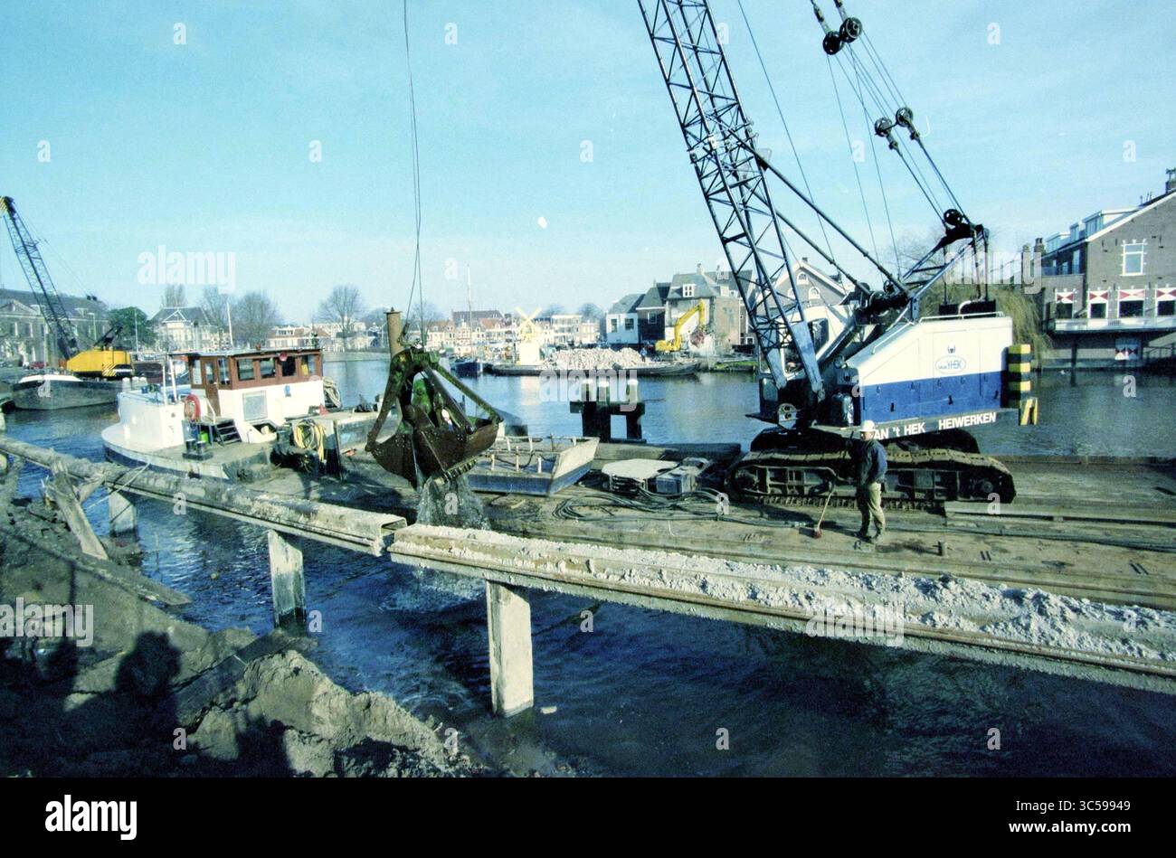 Activités Spaarne, Haarlem, pays-Bas, 12-02-1998 Whizgle News, Dutch Desk, pays-Bas, 1950-2000 Une scène de construction montre de la machinerie lourde au travail sur une jetée, avec une grue soulevant des matériaux pendant que les ouvriers supervisent l'opération. En arrière-plan, les bateaux sont amarrés le long du front de mer, entourés de bâtiments typiques d'une zone portuaire animée. Banque D'Images