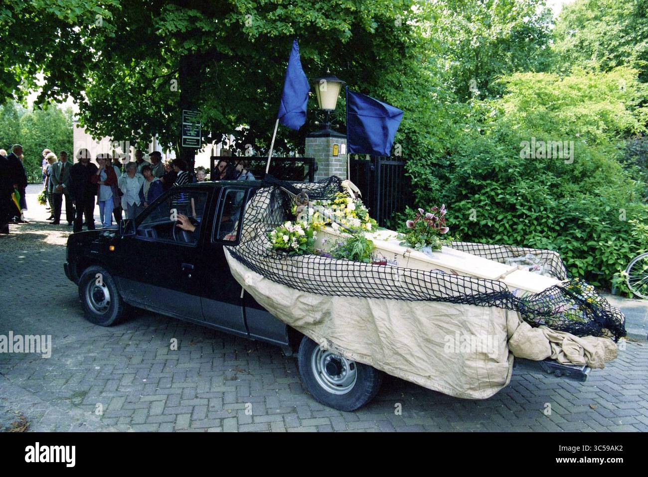 Funeral Frans Verpoorten, Zwanenburg, 01-07-1997 Whizgle News, Dutch Desk, pays-Bas, 1950-2000 Un véhicule décoré orné de drapeaux et d'arrangements floraux est vu se déplacer à travers un rassemblement de spectateurs, entouré d'une végétation luxuriante. La scène transmet un sens de cérémonie ou d'hommage. Banque D'Images