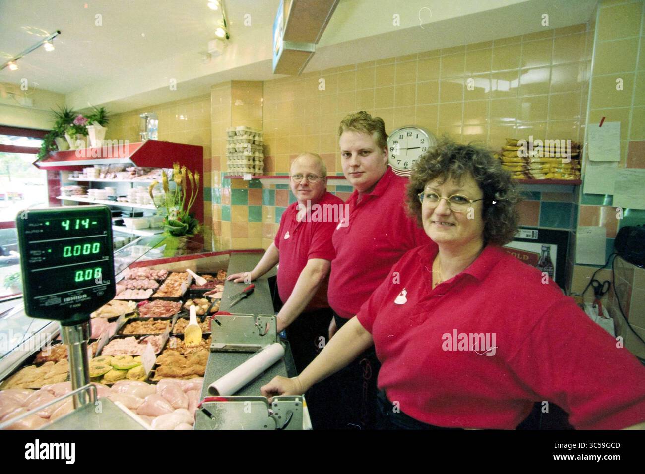 Chicken snack bar Bart, IJmuiden, IJmuiden, pays-Bas, 03-06-1999 Whizgle News, Dutch Desk, pays-Bas, 1950-2000 trois individus souriants se tiennent derrière une exposition de viandes et de produits alimentaires dans un magasin. Chacun porte une chemise rouge vif, et ils semblent prêts à aider les clients, avec une échelle et une horloge visibles en arrière-plan. L'atmosphère est animée et accueillante, mettant en valeur une entreprise locale dynamique. Banque D'Images