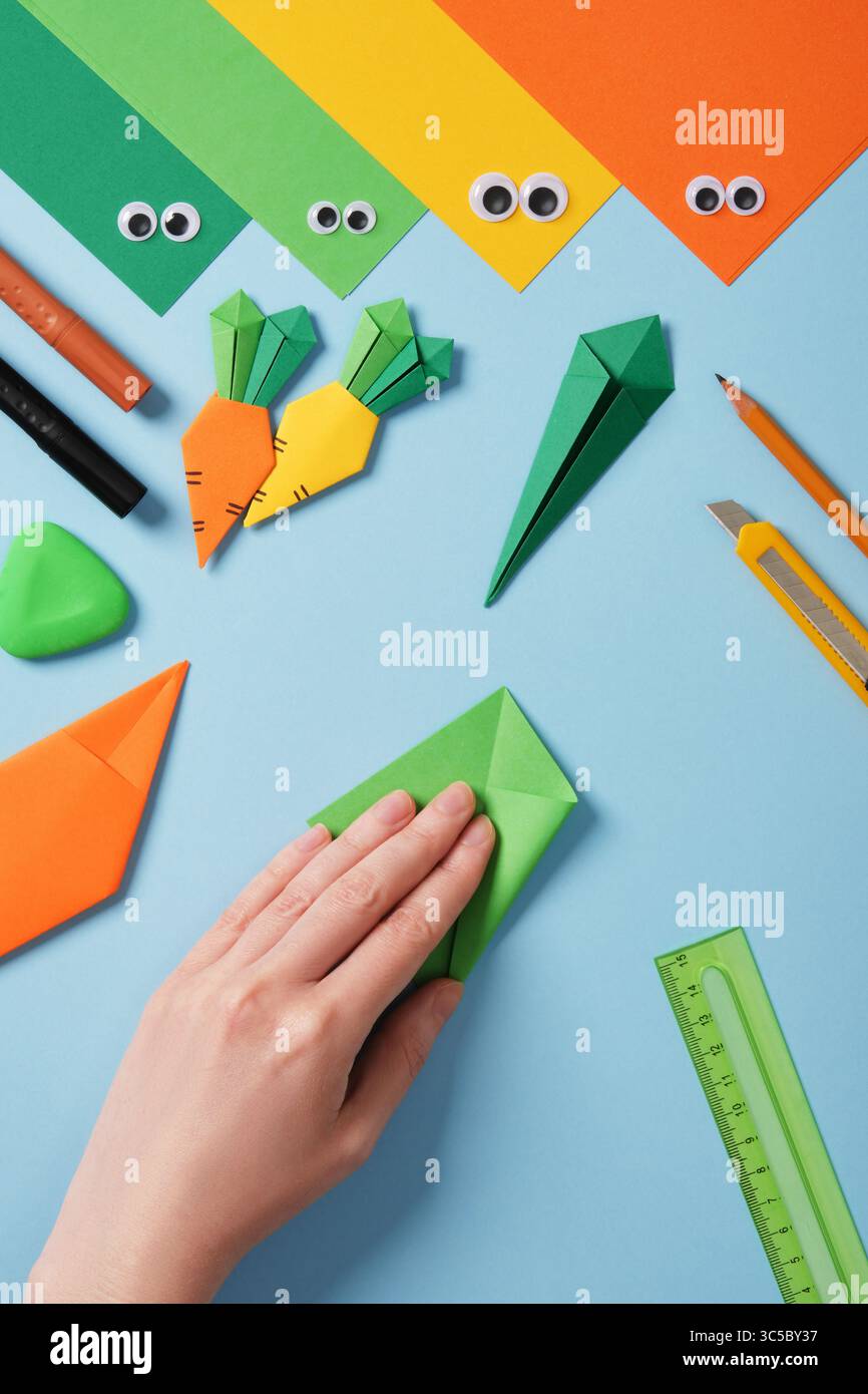 Fabrication de carottes origami. Projet DIY. Pliez les morceaux de papier verts en diagonale. Pliez les bords vers le centre. Banque D'Images