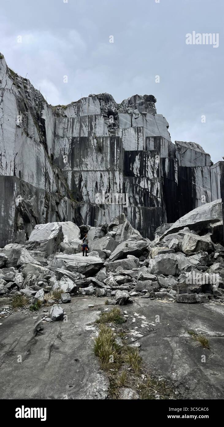 Adventurous Boy se tient au milieu de vastes structures en pierre dans une carrière de marbre abandonnée, entourée de falaises imposantes et d'un terrain accidenté, mettant en valeur le brut Banque D'Images