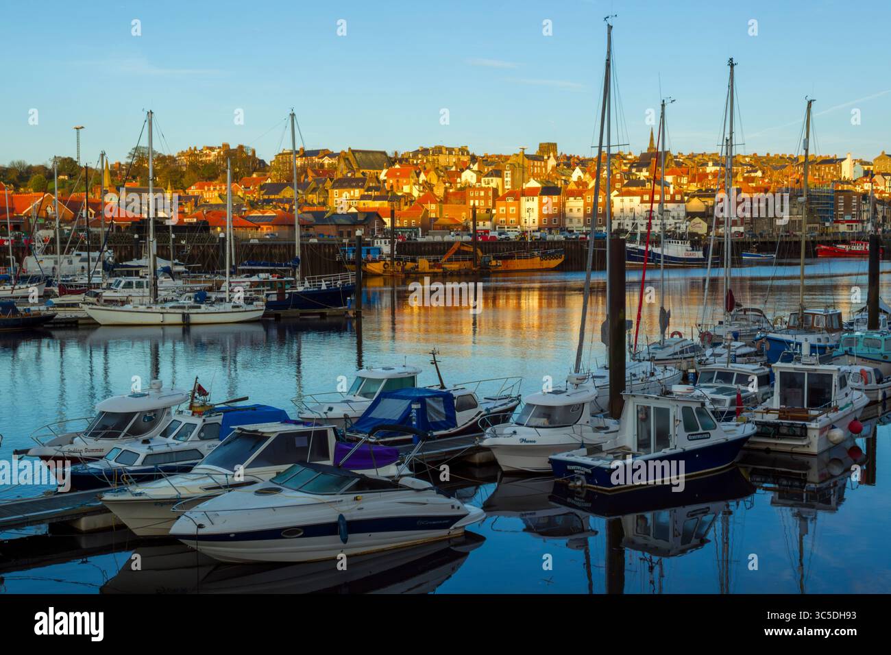 Vue de lumière dorée du matin sur la marina de Whitby avec des bateaux amarrés au premier plan et des bâtiments à flanc de colline en arrière-plan sous un ciel bleu Banque D'Images
