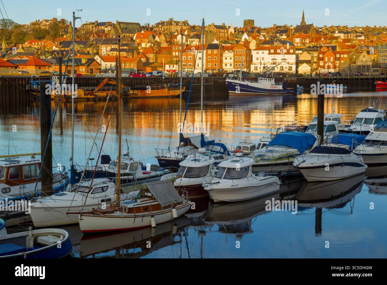 Vue de lumière dorée du matin sur la marina de Whitby avec des bateaux amarrés au premier plan et des bâtiments à flanc de colline en arrière-plan sous un ciel bleu Banque D'Images