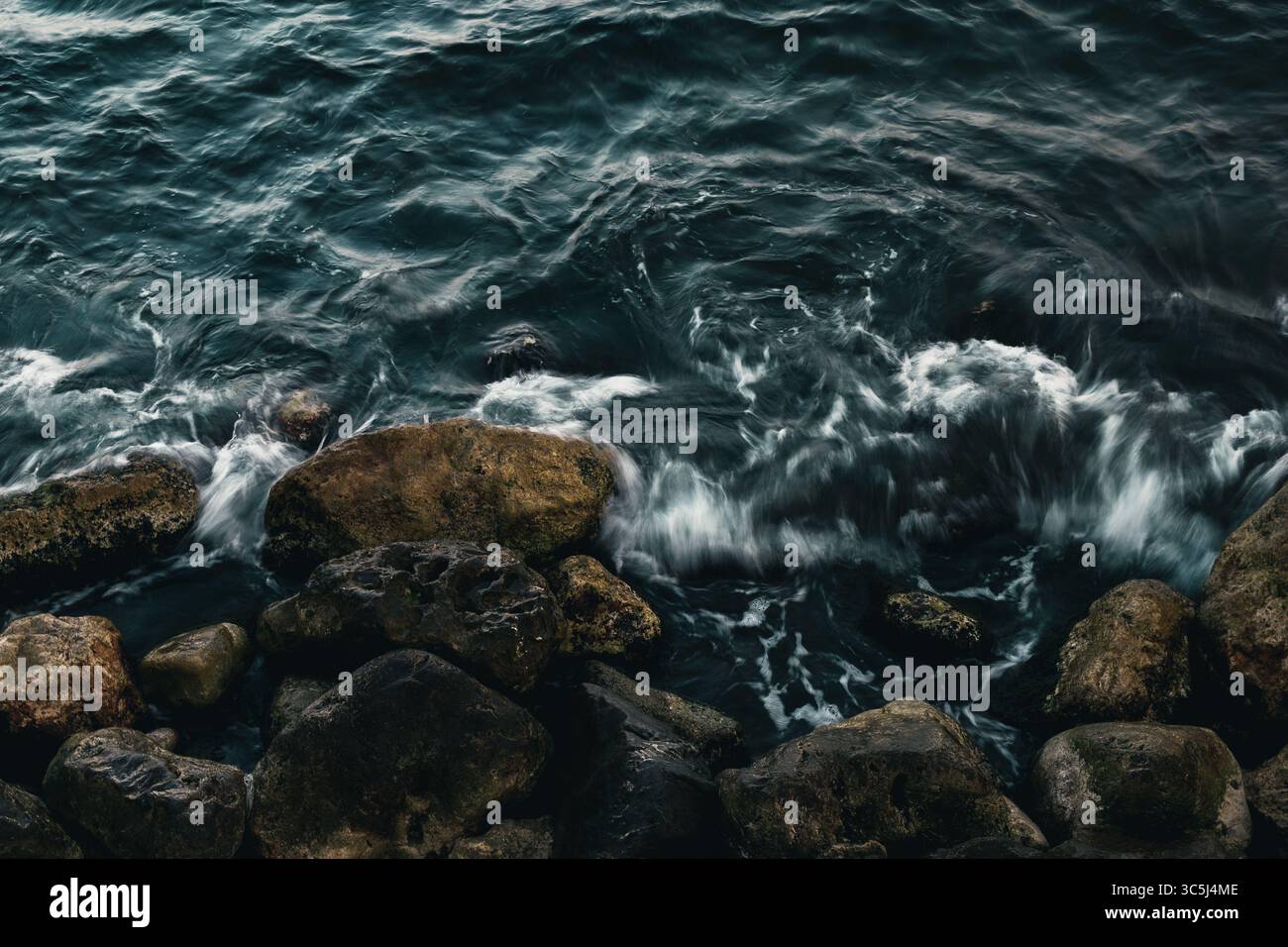 Des vagues dynamiques s'écrasent contre des rochers accidentés, créant une scène côtière spectaculaire et puissante. Banque D'Images