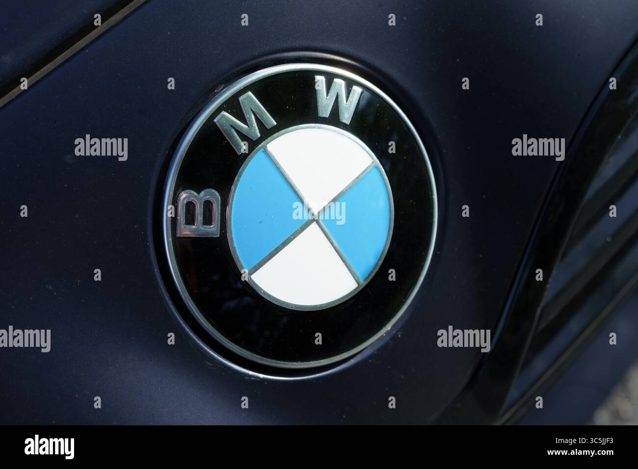 Gros plan d'un logo BMW sur un véhicule sombre, montrant le cercle bleu et blanc avec garniture chromée. Banque D'Images