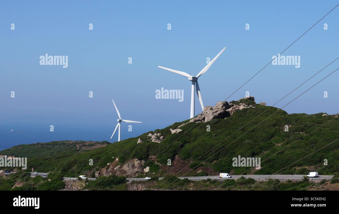 Les éoliennes blanches tournent sur une colline verdoyante surplombant une autoroute côtière et la mer bleue Banque D'Images