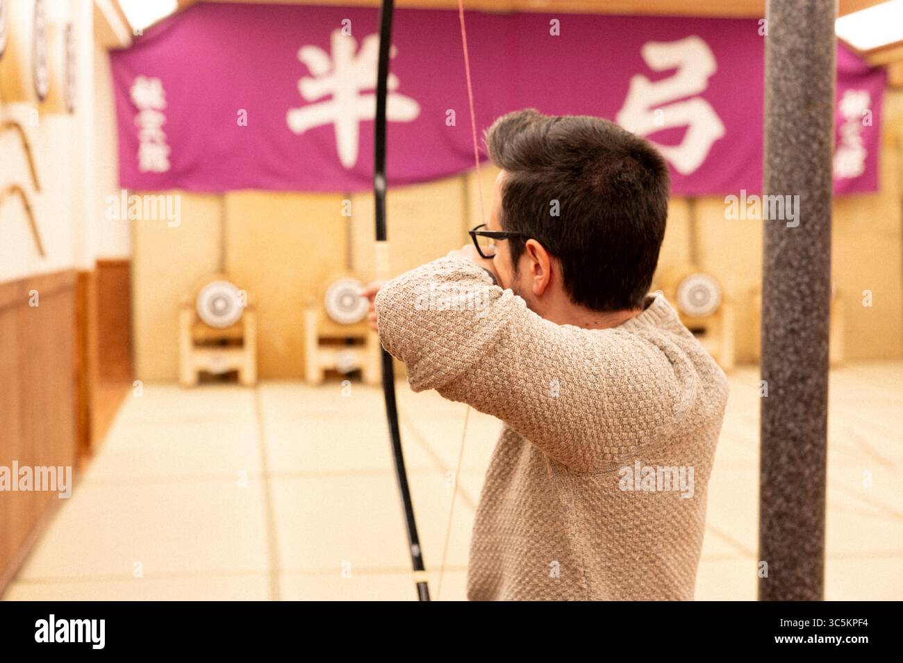 Homme pratiquant le tir à l'arc japonais traditionnel (Kyudo) en intérieur au Japon Banque D'Images