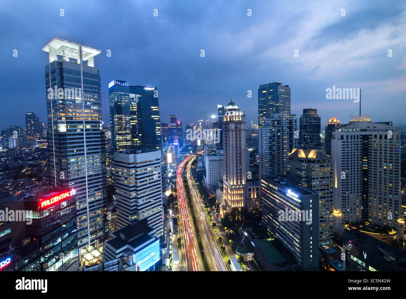 Vue aérienne nocturne du quartier central des affaires de Jakarta, avec gratte-ciel illuminés et feux de circulation animés le long d'une avenue principale. Banque D'Images