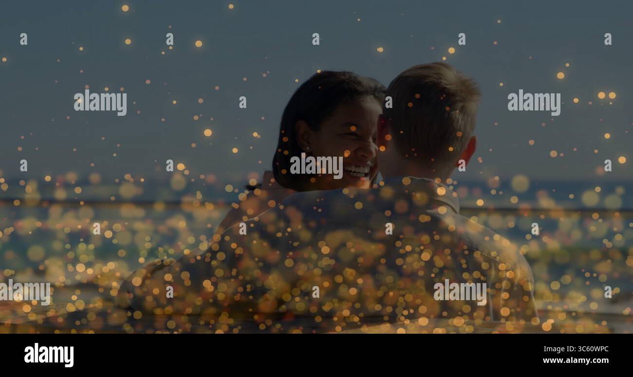 Femme souriante embrassant l'homme sur le pont au bord de l'eau, avec garde-corps en métal et lumières bokeh dorées Banque D'Images