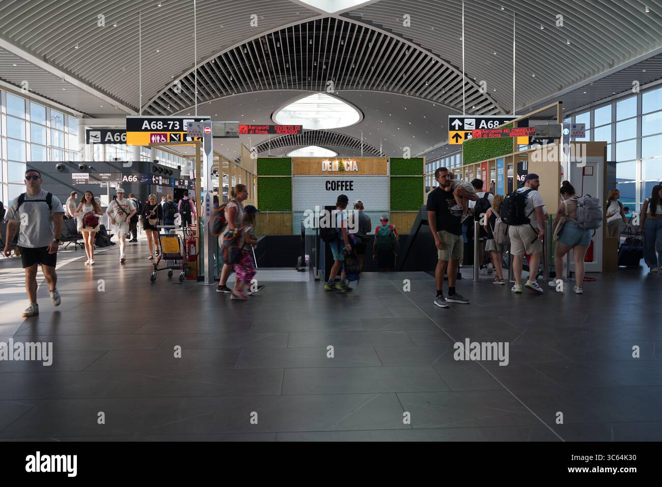 À l'intérieur de l'aéroport Fiumicino de Rome, les passagers traversent un terminal lumineux avec de hauts plafonds en direction des zones d'embarquement, des boutiques et des points de transit. Banque D'Images