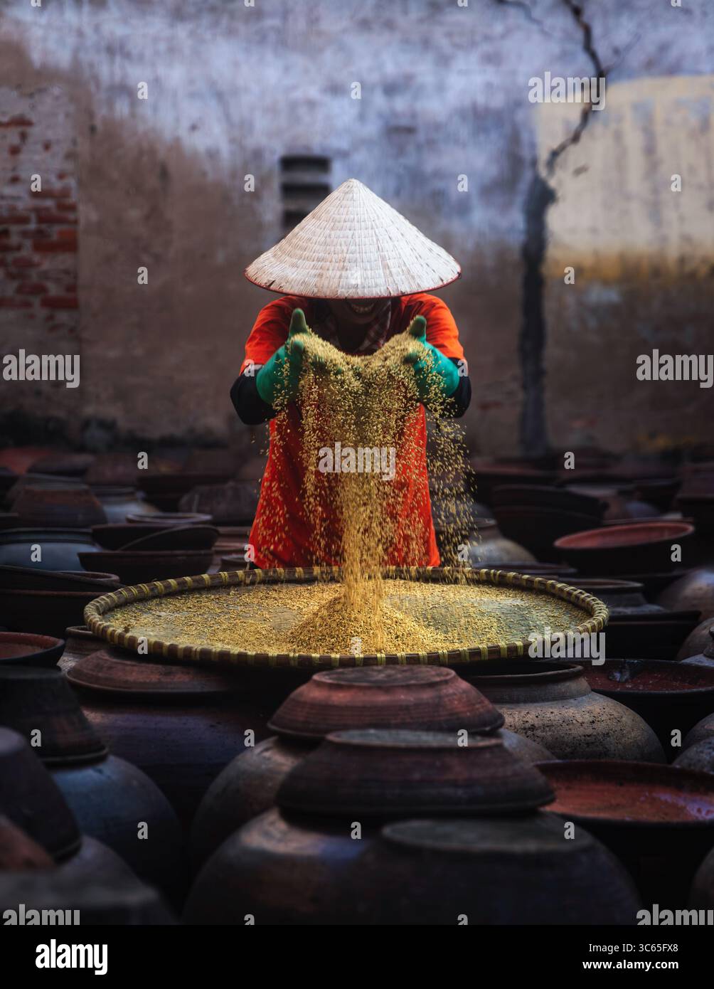 Hanoi, Vietnam - 09 avril 2024 : vue d'un ouvrier portant un chapeau conique traditionnel tamisant des grains d'or au-dessus de rangées de pots de terre, créant une scène Banque D'Images