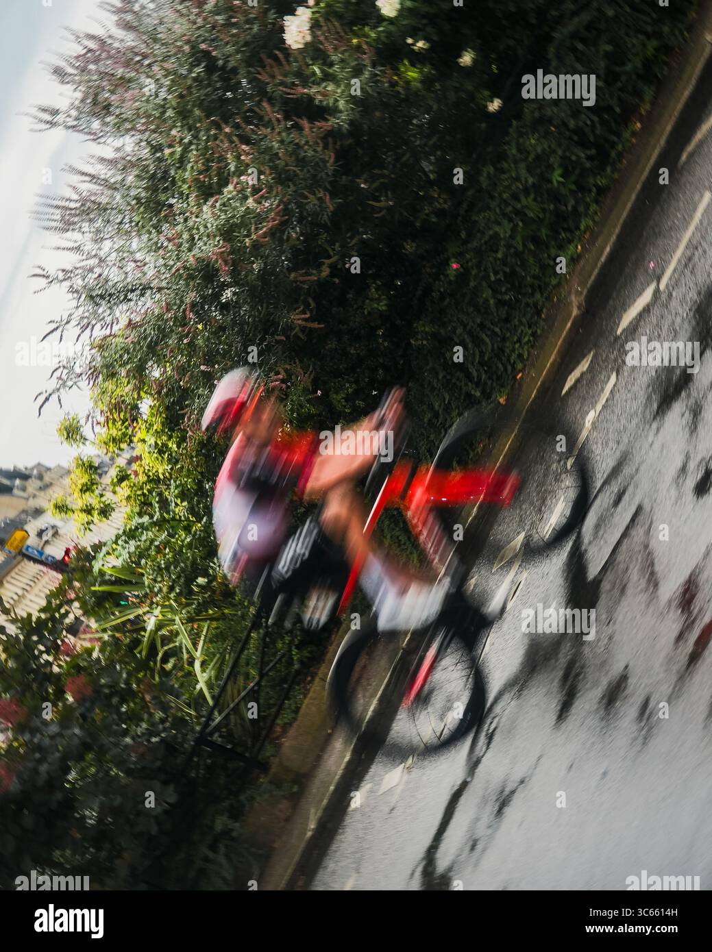 Paris, France - 27 juillet 2025 : vue d'un cycliste du Tour de France 2025 qui passe à grande vitesse devant une végétation luxuriante, un flou de mouvement contre l'asph baigné de soleil Banque D'Images