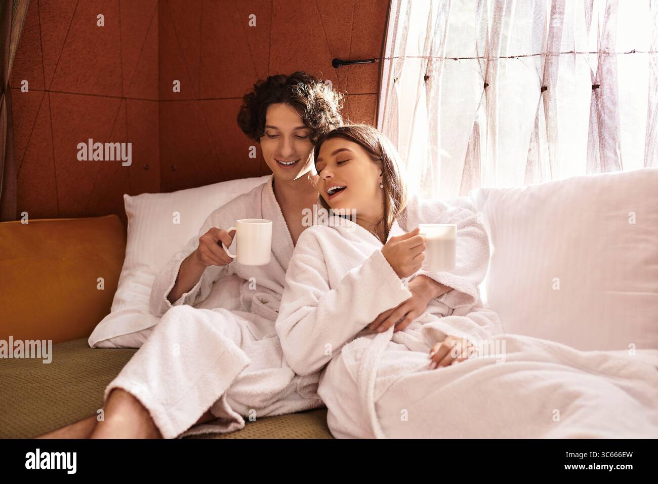 Aimer les câlins de couple sur un canapé confortable tout en partageant des boissons chaudes et des rires. Banque D'Images