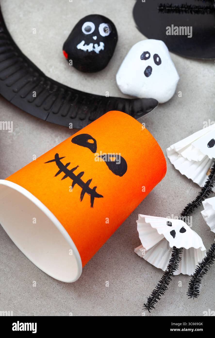 Citrouille d'Halloween faite à partir d'une tasse de papier orange avec des fantômes de roche derrière, et quelques fantômes d'emballage de cupcake Banque D'Images