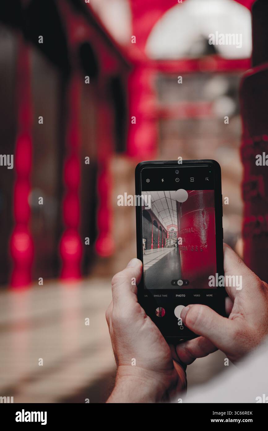 Porto, Portugal - 17 juin 2022 : vue des mains tenant un smartphone capturant l'escalier rouge éclatant, sa surface brillante réfléchissant la lumière, créant un contraste dynamique sur l'arrière-plan flou. Banque D'Images