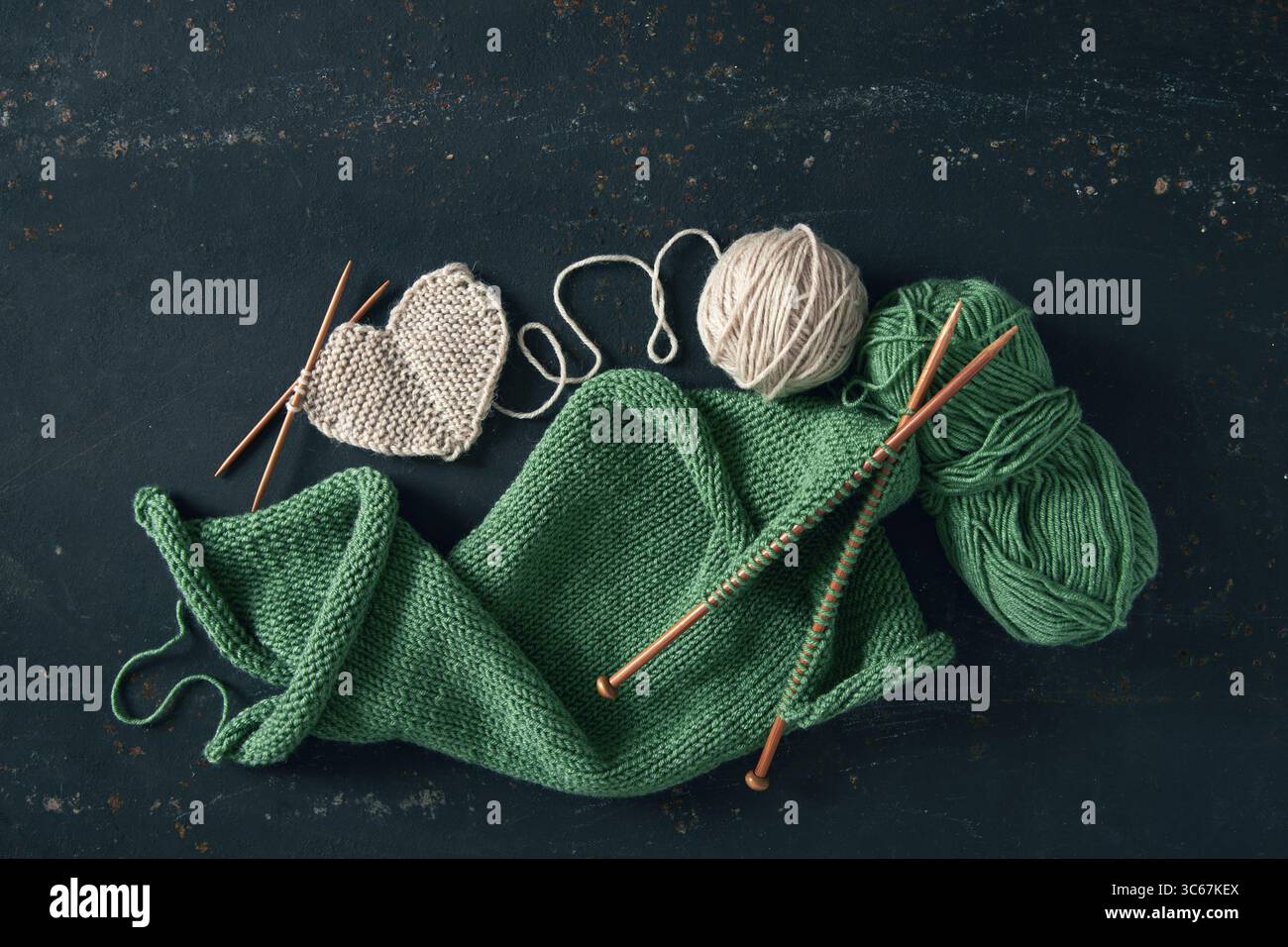 Projet de tricot avec de la laine blanche et verte et des aiguilles de bambou sur fond rustique. Projet de tricot incomplet avec des aiguilles en bois. Banque D'Images