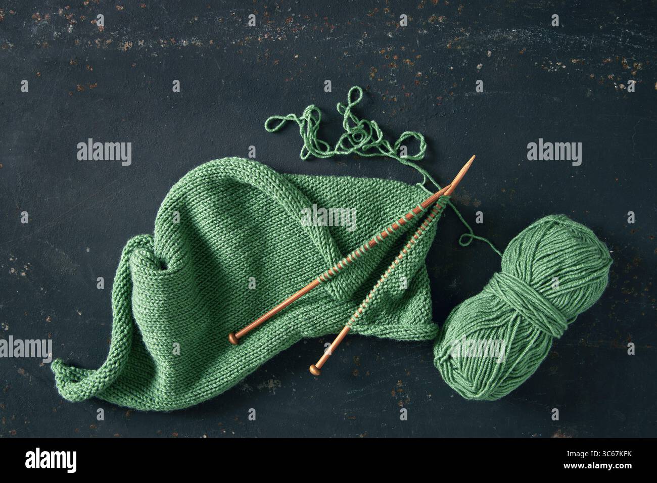 Projet de tricot avec de la laine verte et des aiguilles de bambou sur fond rustique. Projet de tricot incomplet avec des aiguilles en bois. Banque D'Images