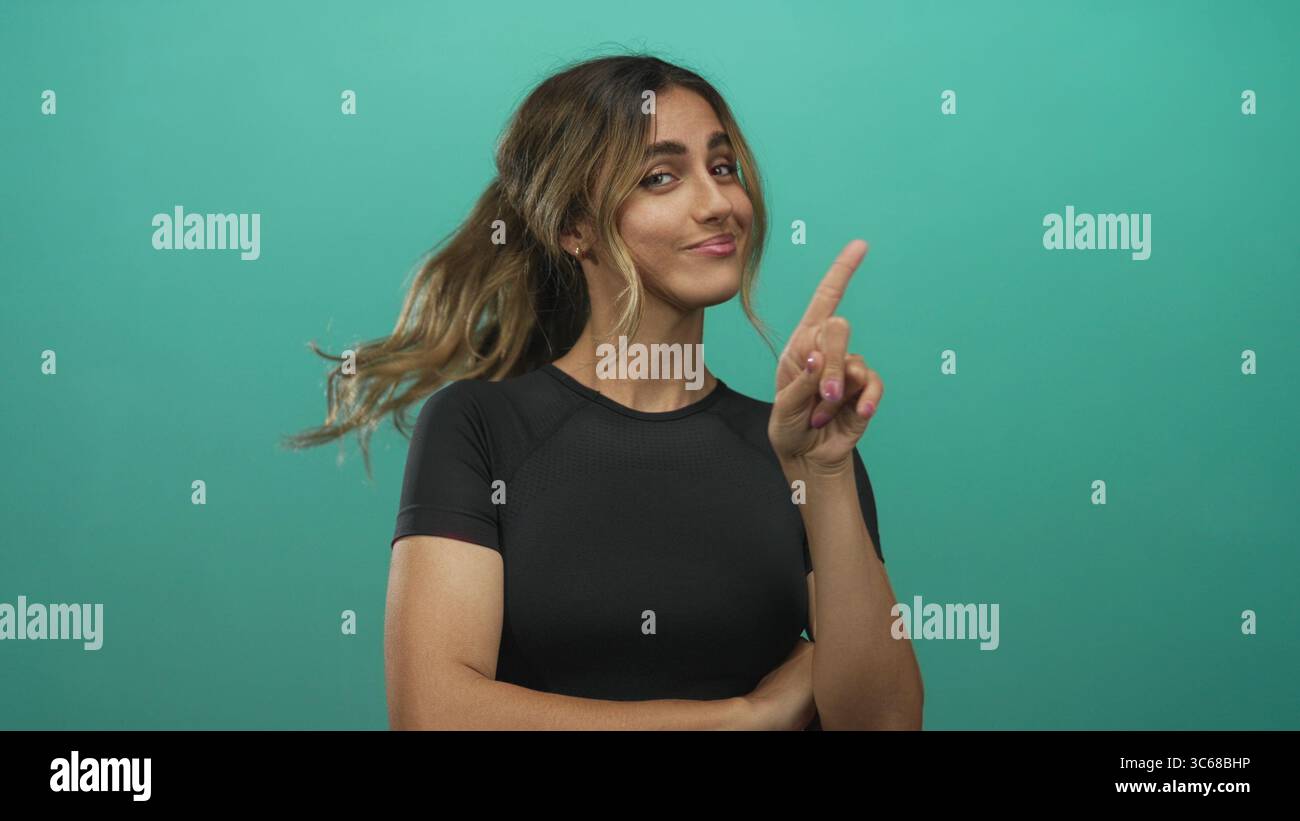 Jeune femme blonde pointe le doigt vers le haut dans un studio photo vert ; confiance ludique motivation autonomisation. Banque D'Images