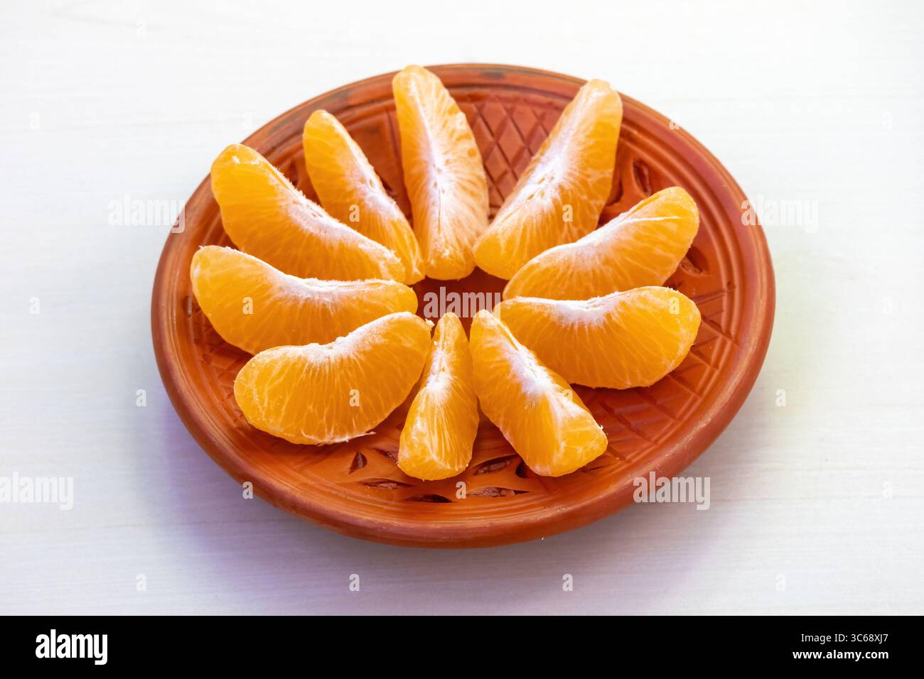 Une orange douce juteuse et pelée et ses succulents segments, présentés sur une assiette en argile. Banque D'Images Une orange douce juteuse et pelée et ses succulents segments, présentés sur une assiette en argile. Banque D'Images