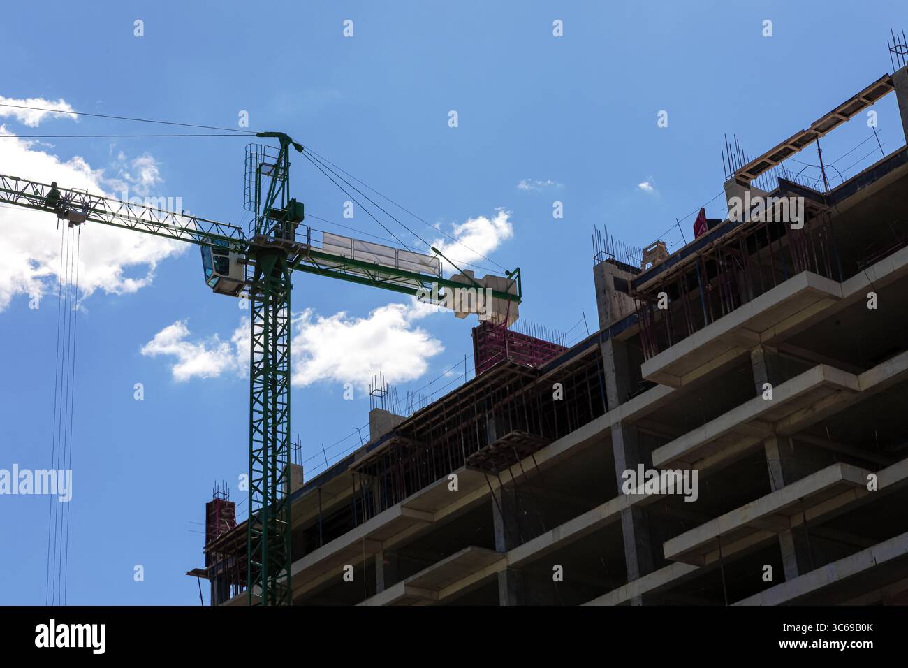 Vue en angle bas d'un bâtiment en béton en construction avec une grue à tour verte contre un ciel bleu vif avec des nuages. Banque D'Images