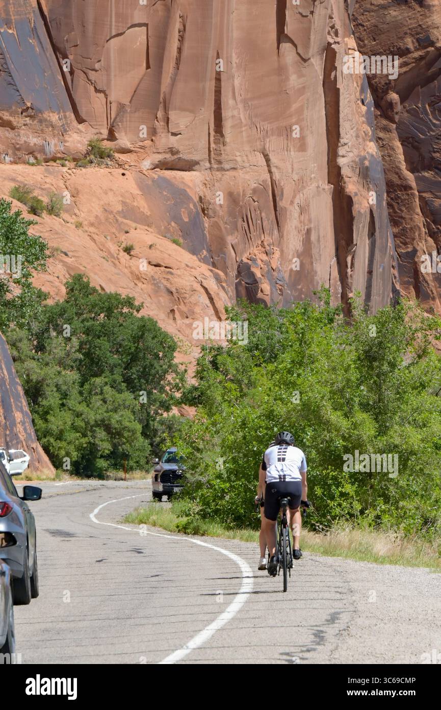 Moab, Utah, États-Unis - 25 mai 2025 : cycliste à vélo sur Potash Road sous d'énormes rochers près de Moab avec le passage de la circulation Banque D'Images